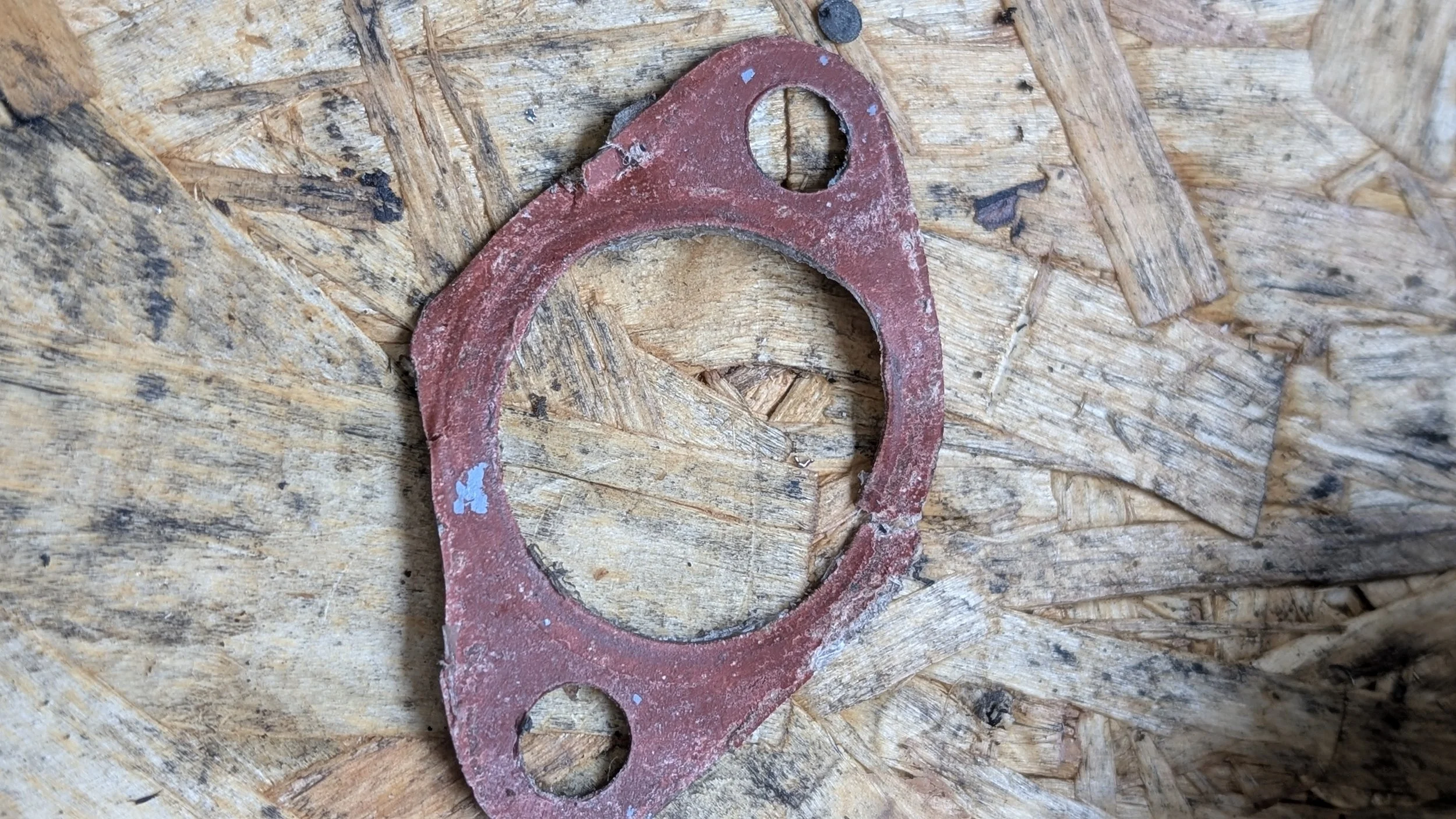 A rusty, red-painted metal gasket or washer lying on a rough, wooden surface with visible grain and imperfections.