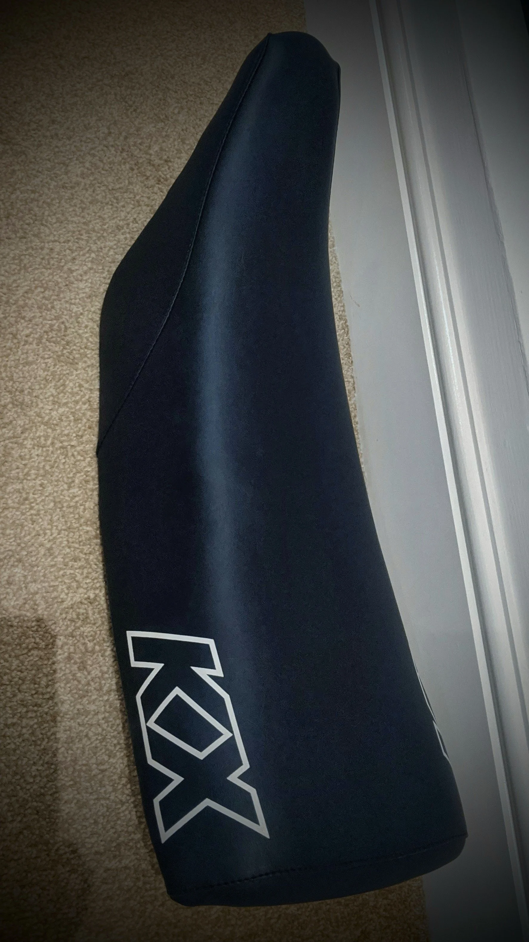 A black foam roller with the XOXX logo on its side, laying on a carpeted floor near a door.