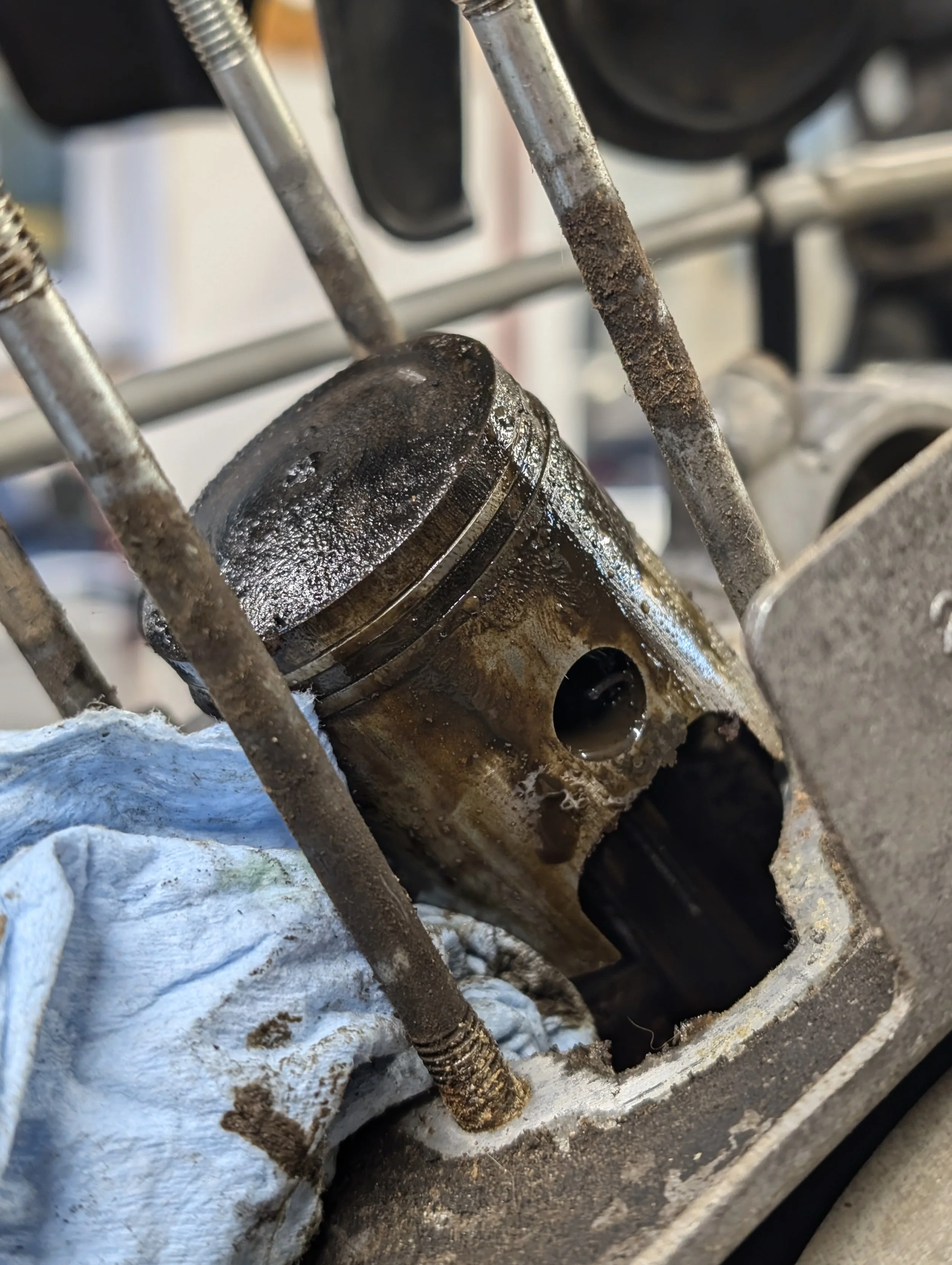 Close-up of a worn piston inside a dirty and rusted engine cylinder, with connecting rods and engine components visible.