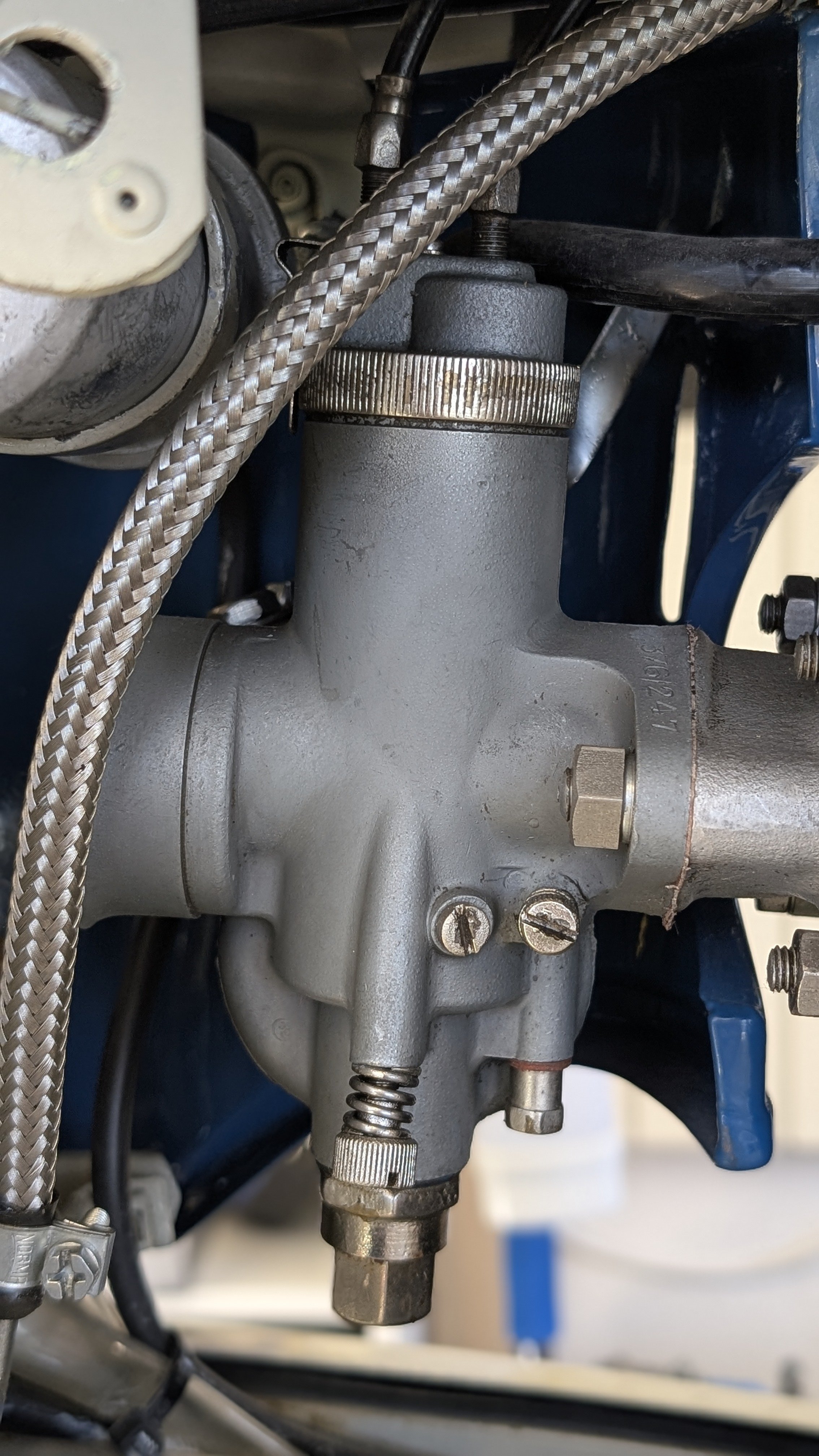 Close-up of a vintage carburetor with metal hoses and screws.