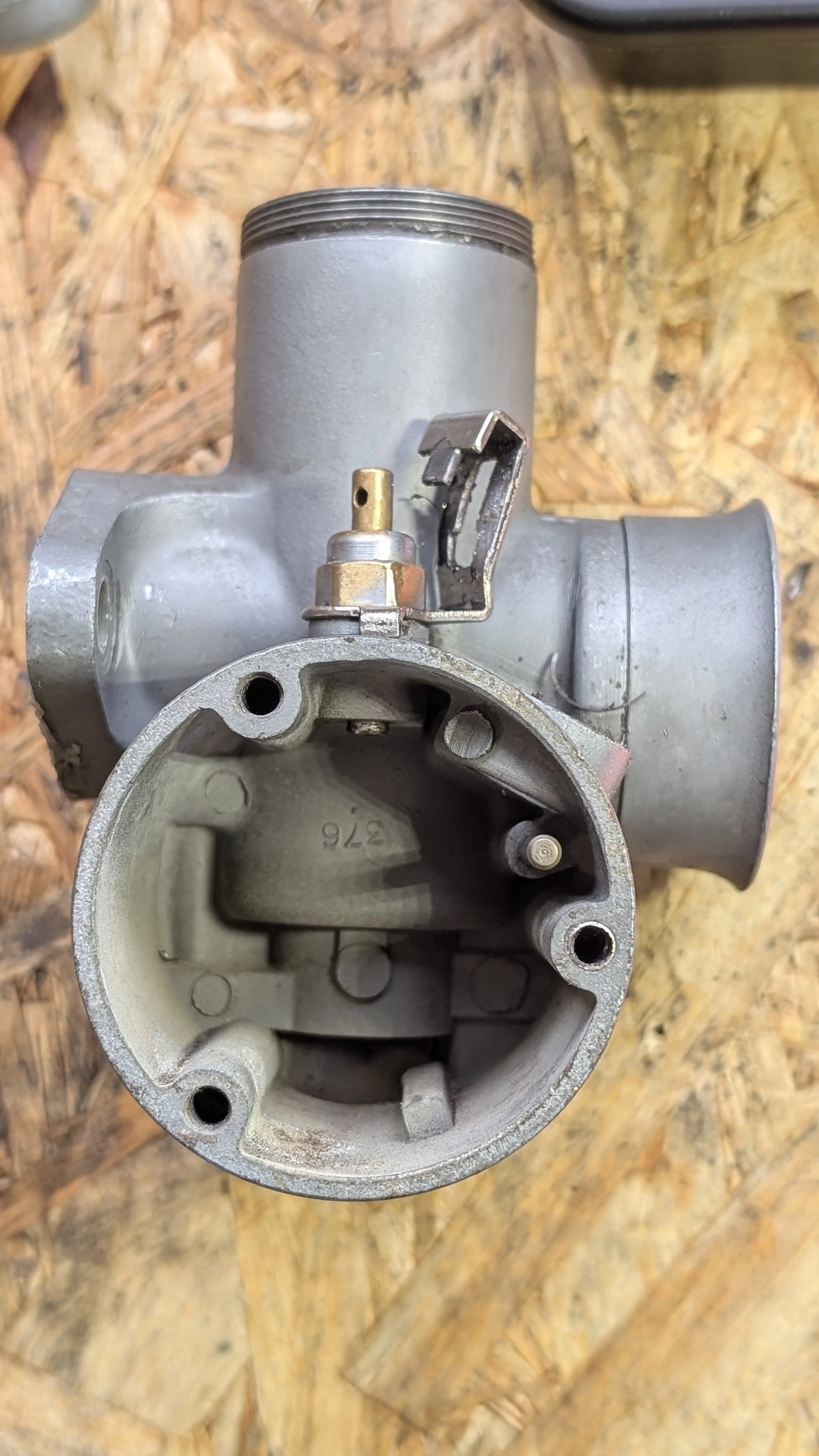 Close-up view of a carburetor with the top and internal parts visible, placed on a wooden surface.