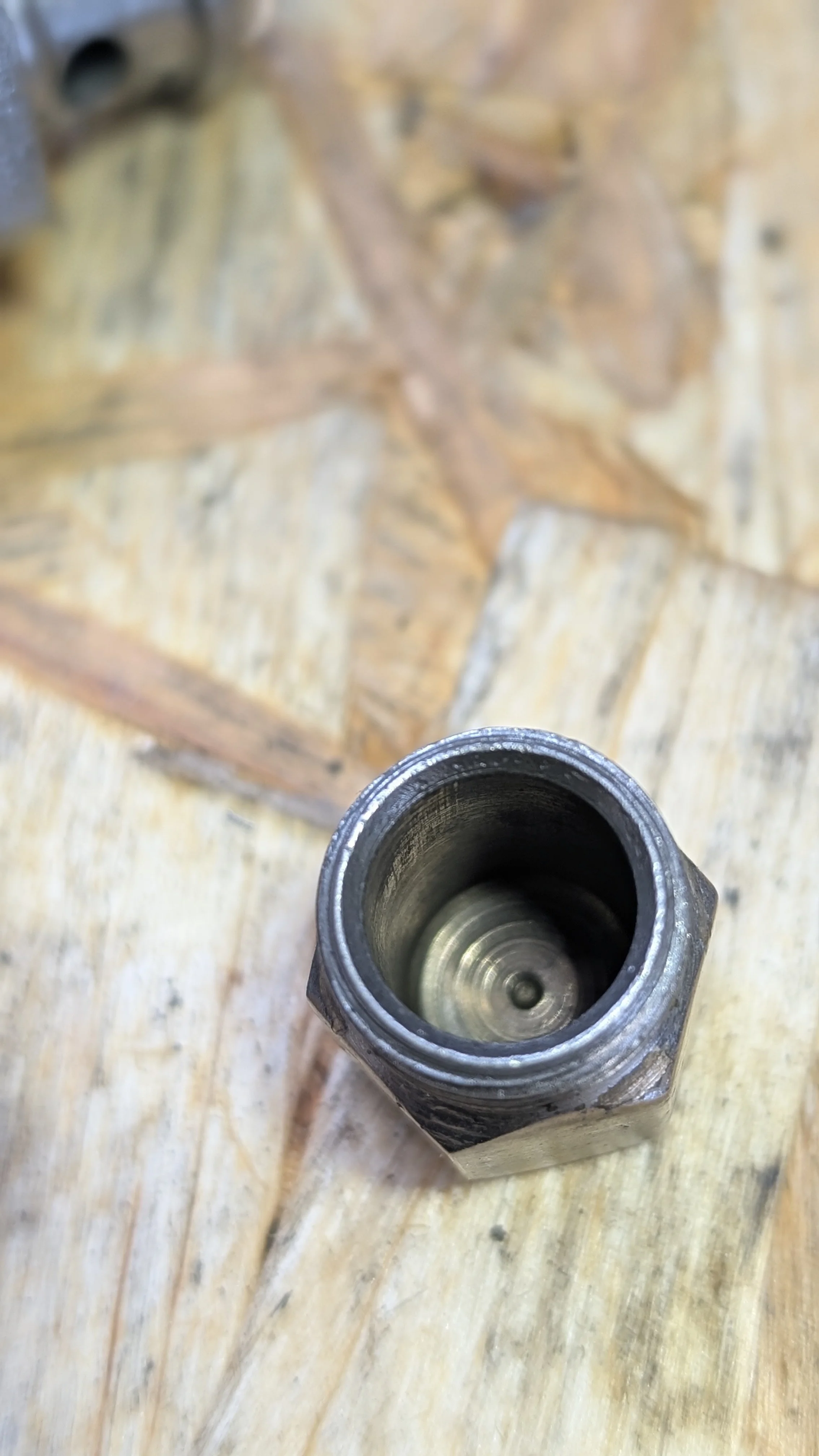 Close-up view of a metal valve component on a wooden surface, with a purple and brown leaf in the background.