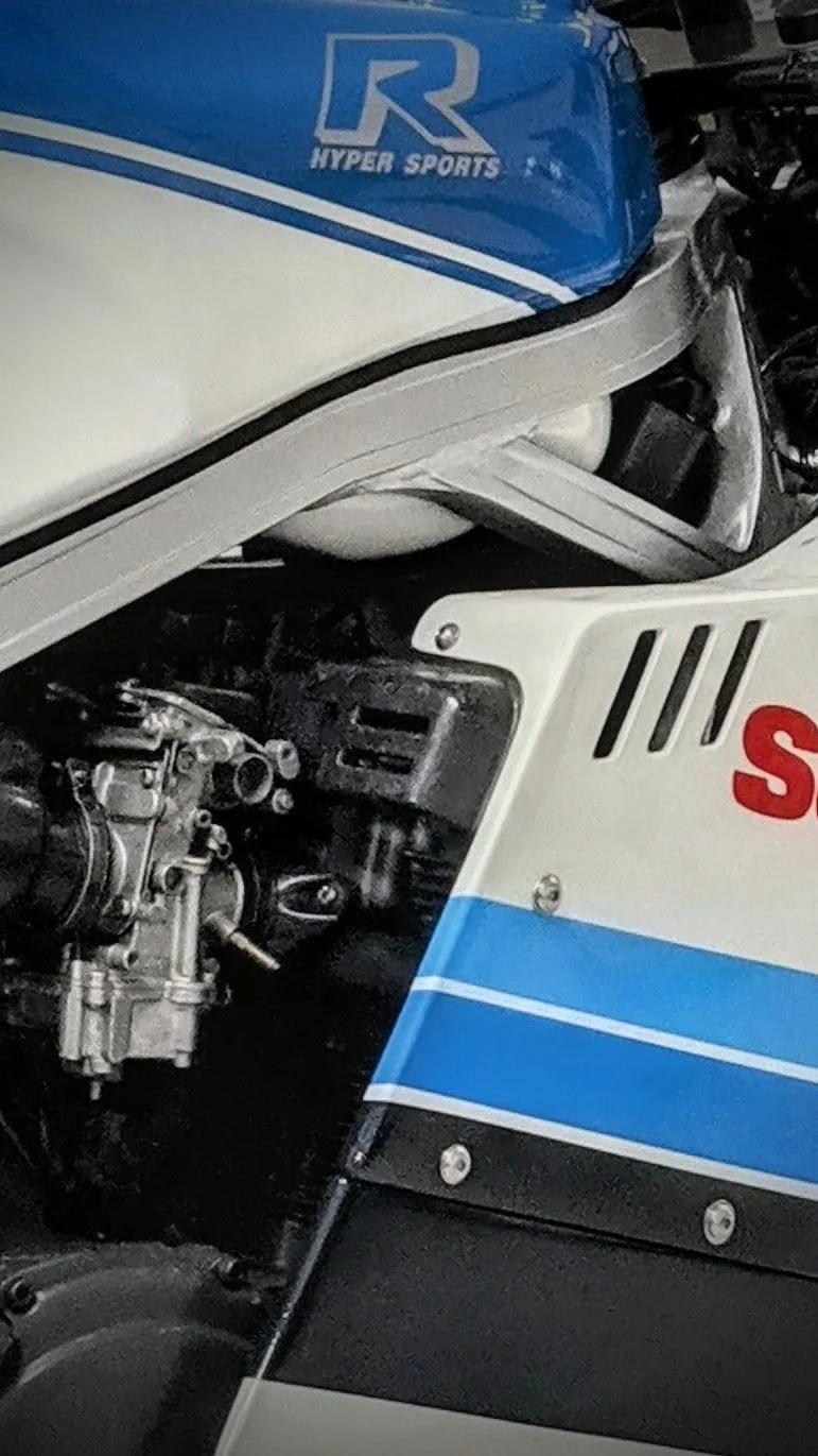 Close-up of a racing motorcycle showing part of the engine and bodywork, with a blue and white color scheme and a graphics logo reading 'R Hyper Sports'.