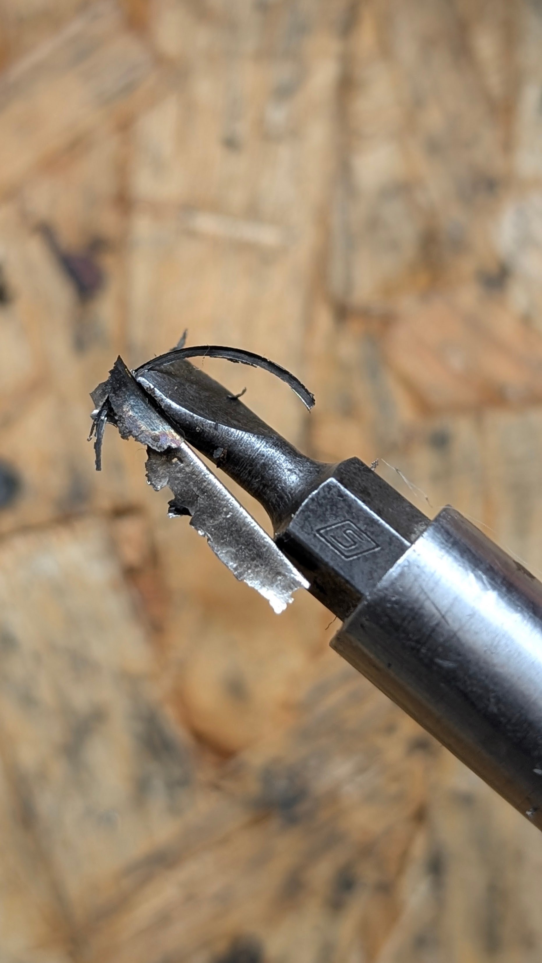 A damaged black ballpoint pen with a broken tip and shredded paper around it, placed on a wooden surface.