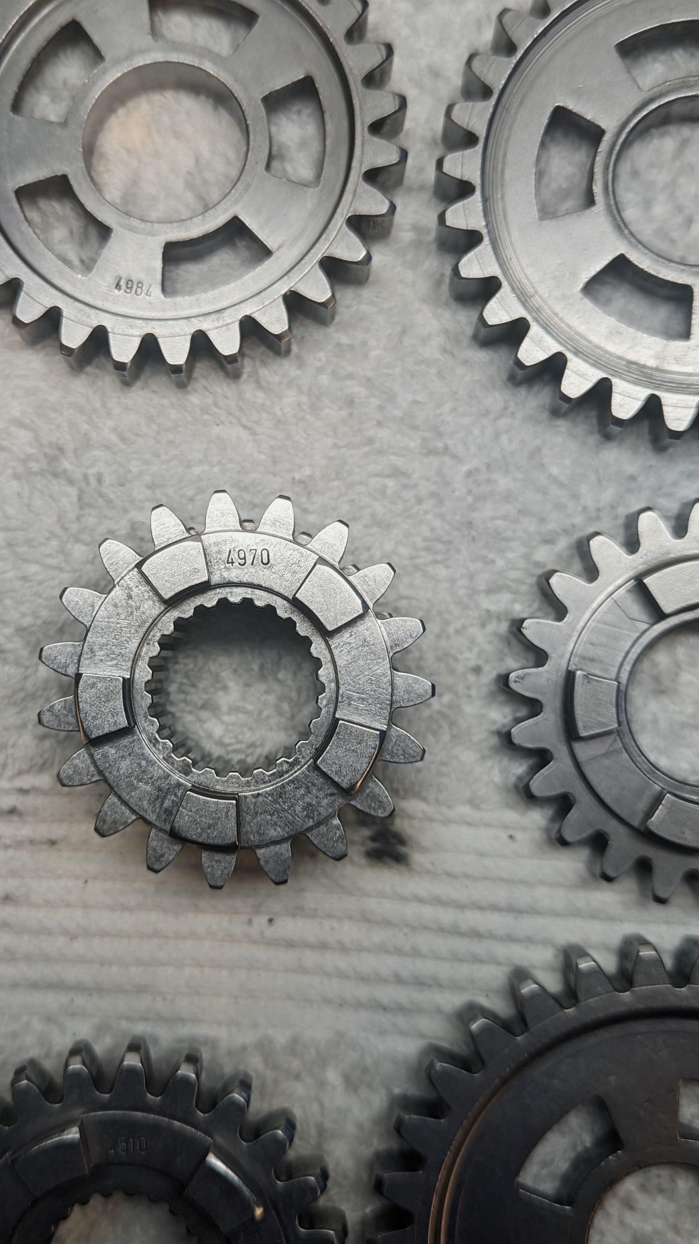 Several metal gears of different sizes with teeth around their edges are displayed on a light-colored surface.