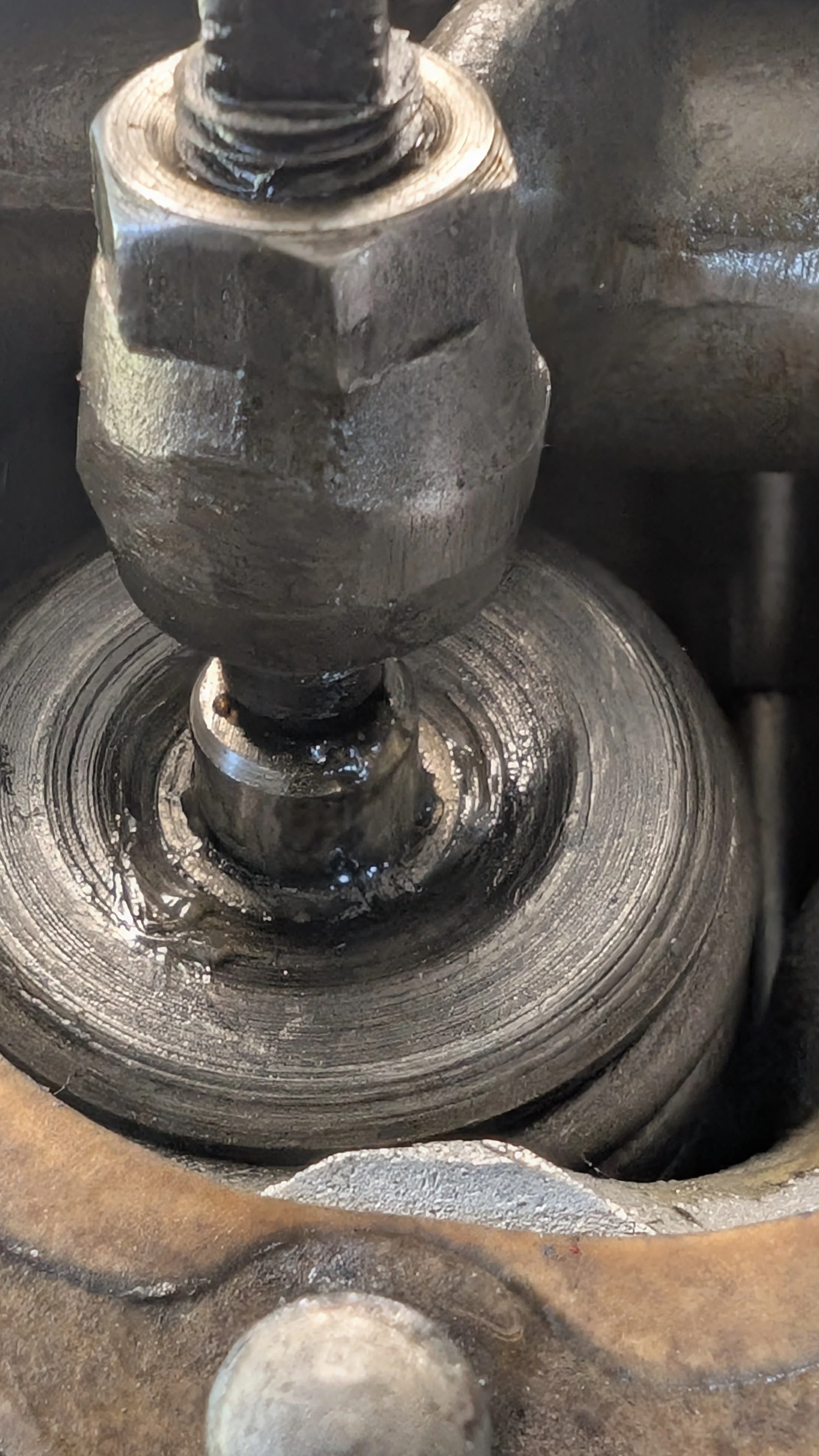 Close-up of a metal valve or screw component with oil or lubricant around it, mounted on a metallic surface.
