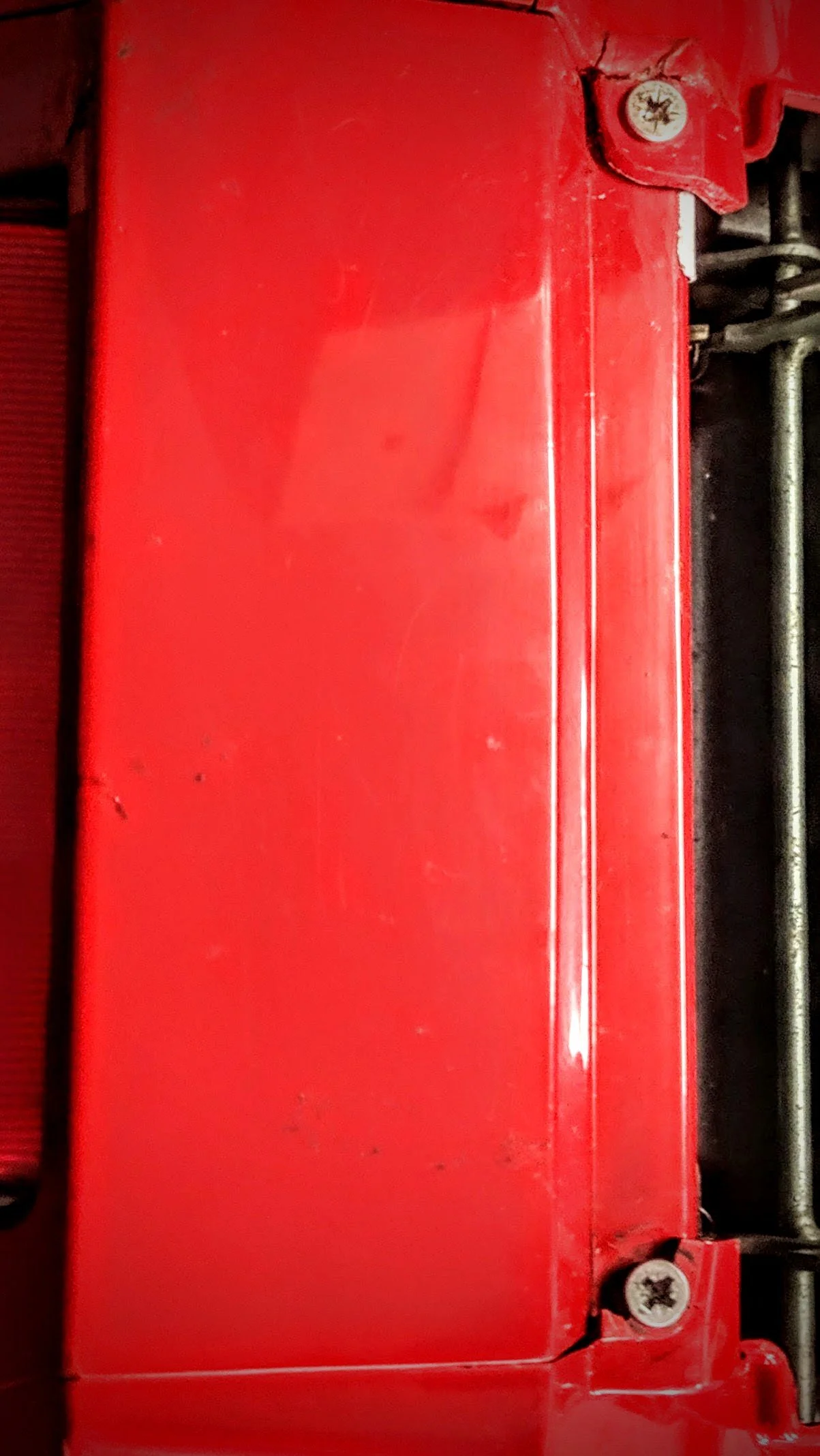Close-up of a red metal surface with visible screws and slight scratches.
