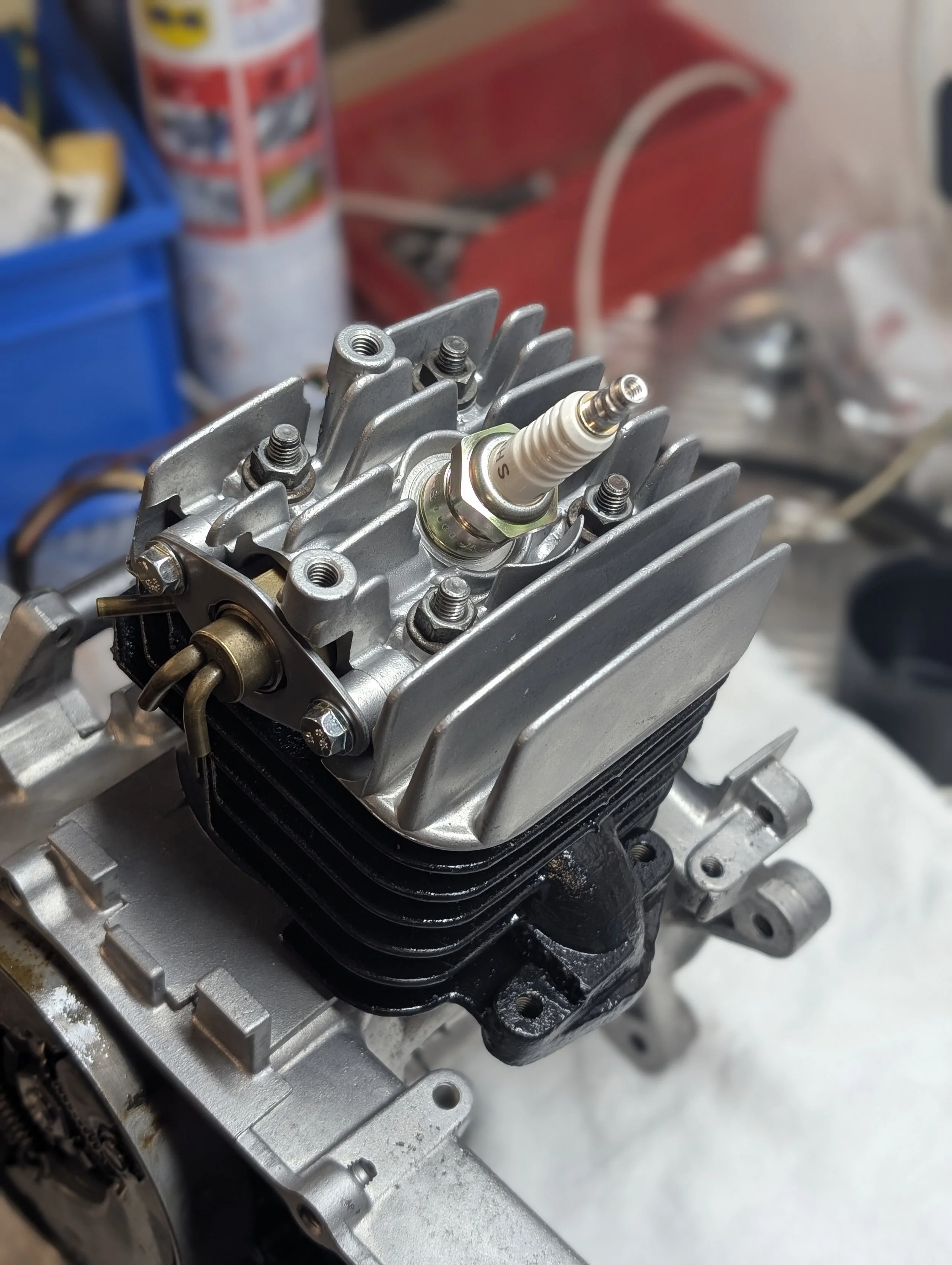 Close-up of a small engine or mechanical component, with visible spark plug and cooling fins.
