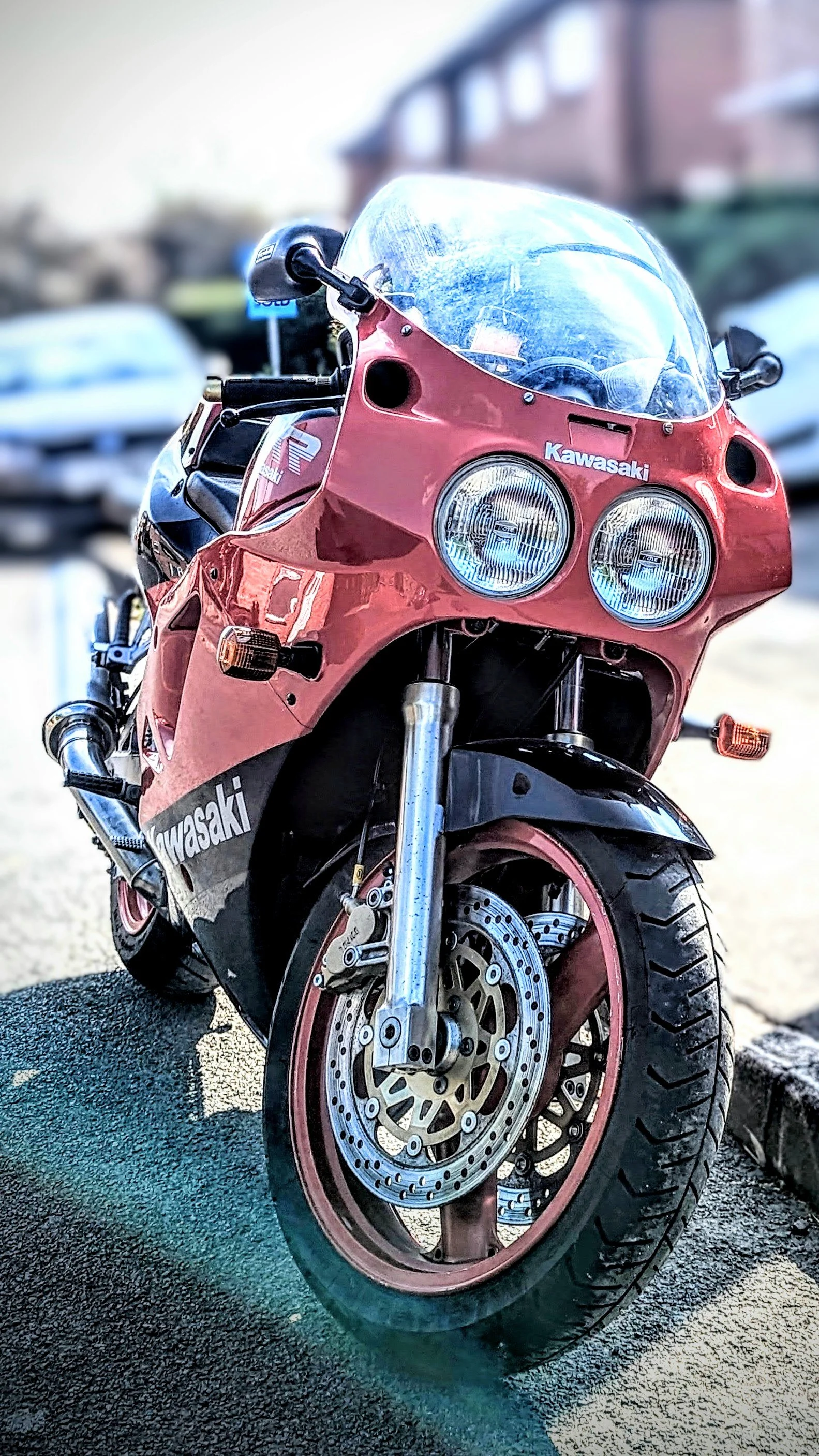 Red Kawasaki sport motorcycle parked on a street with blurred cars in the background.