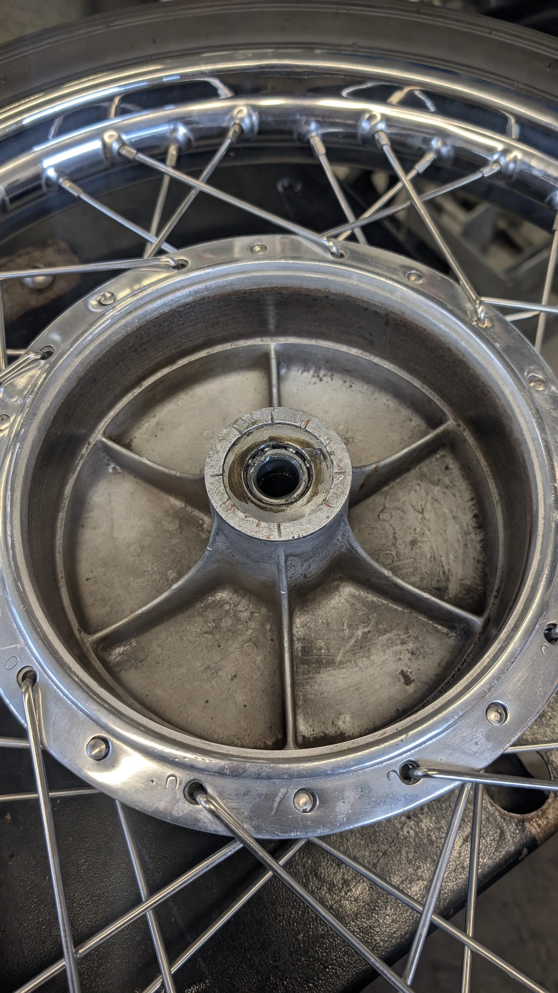 Close-up of a motorcycle or bicycle wheel with spokes and a metal hub, showing dirt and wear.