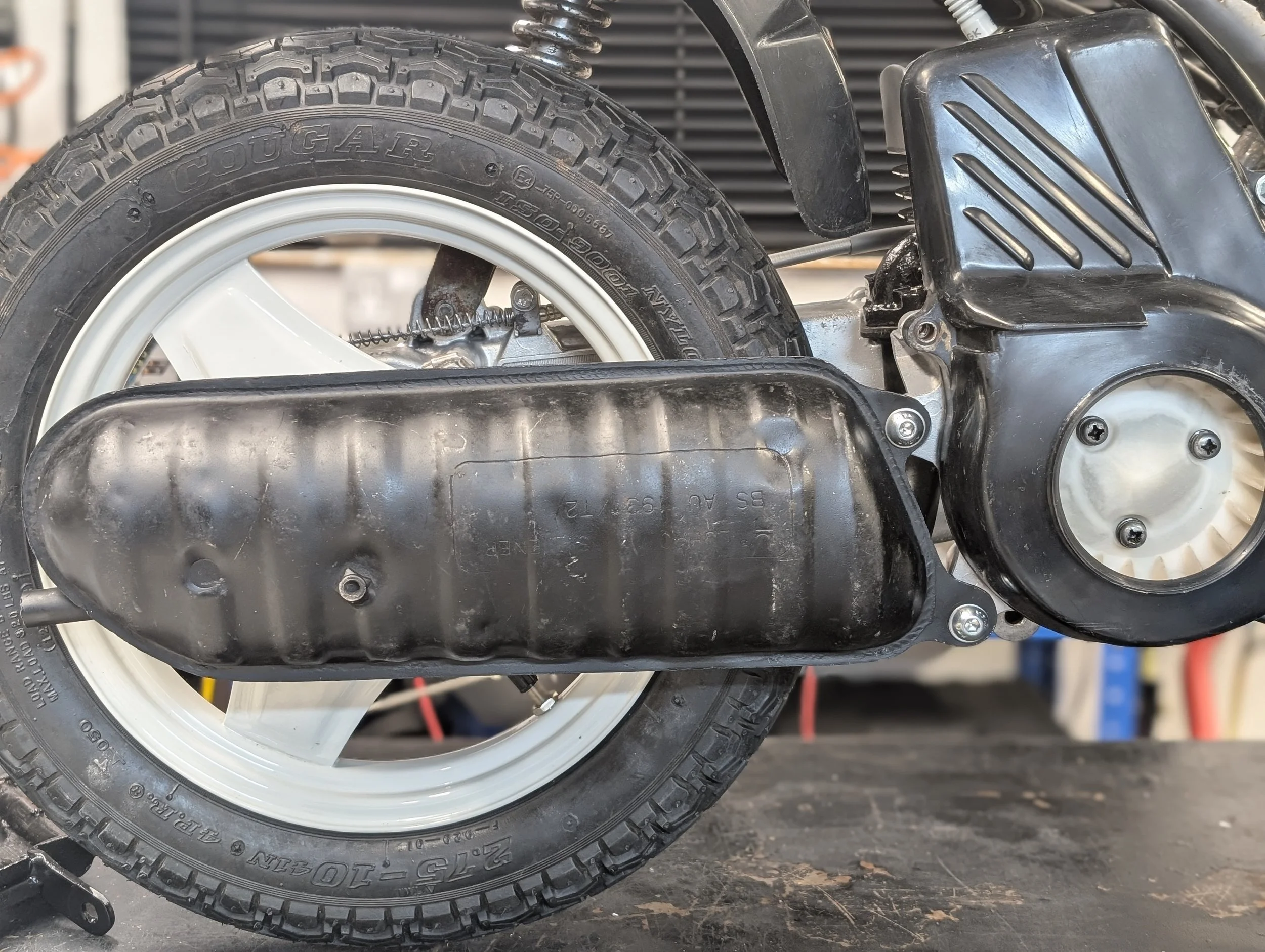 Close-up of a motorcycle rear wheel and exhaust system, showing a tire with the brand 'Dunlop' and model 'Street Response', and part of the metal chassis and suspension.