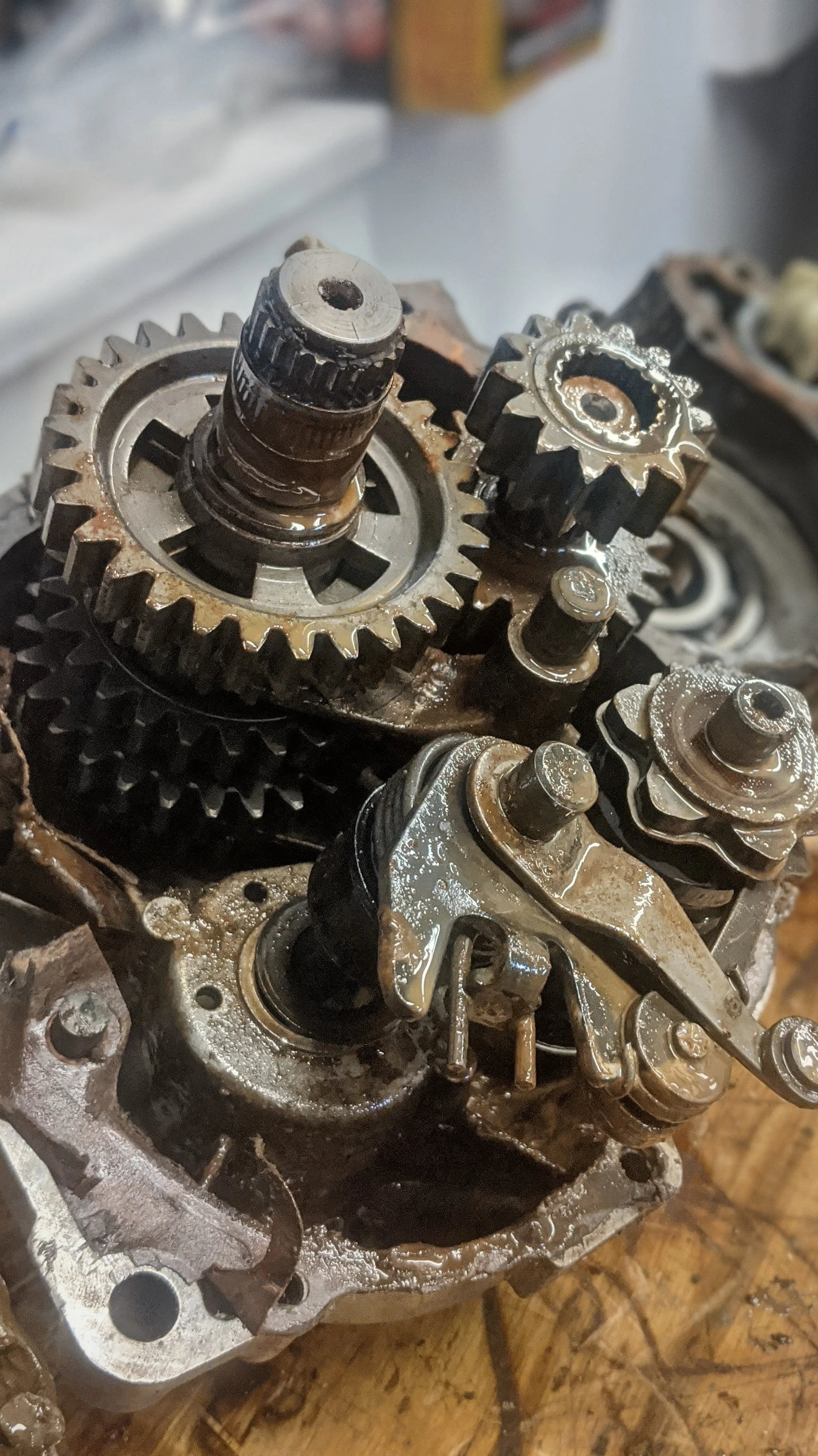Close-up of worn mechanical gears, shafts, and components inside an engine with oil and rust.