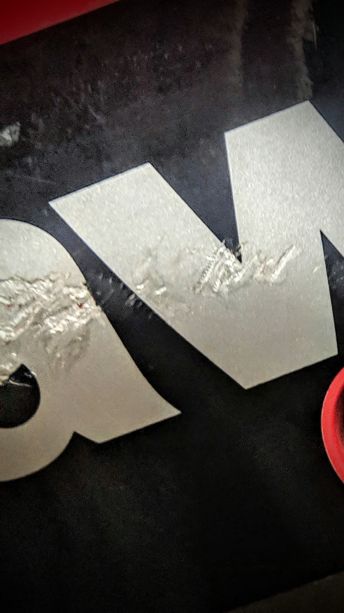 Close-up of a poster or printed material with a black background and white text, showing the characters "t" and part of another letter, with a red circular object partially visible on the right side.