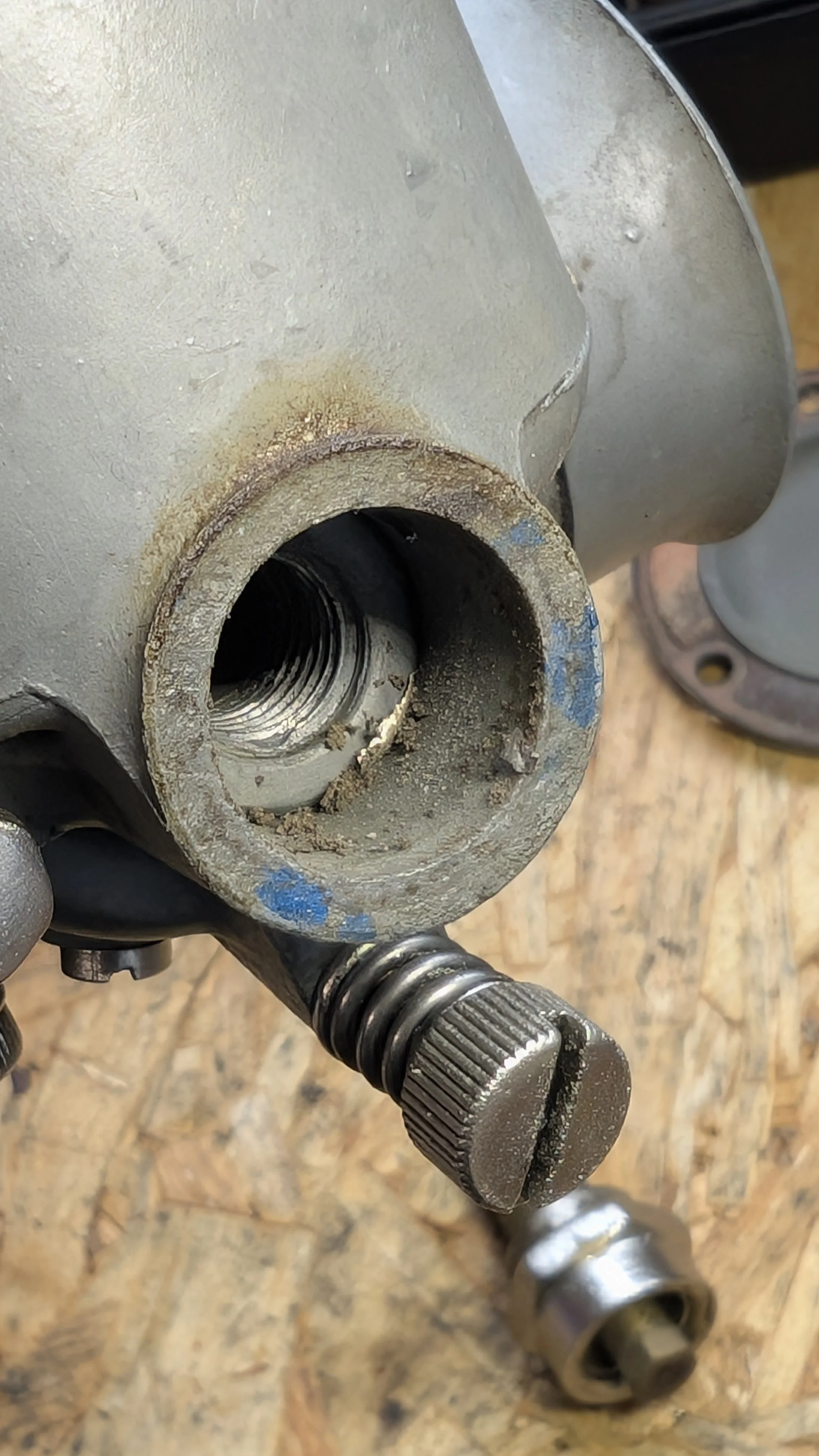 Close-up of a metallic mechanical part with a threaded hole, some dirt, and a tool with a splined end nearby on a wooden surface.