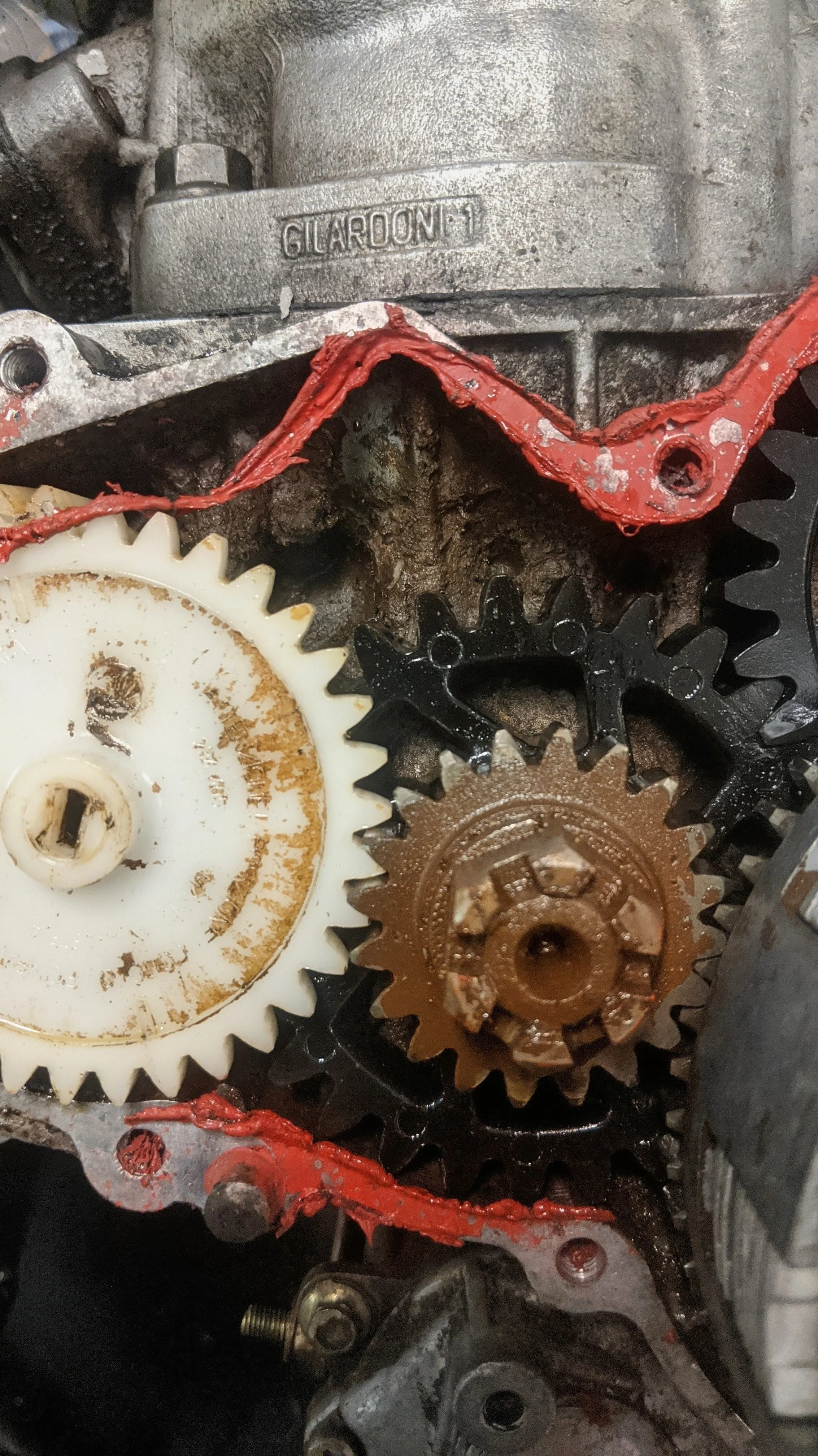 Close-up of a mechanical gear system with gears of different sizes, some rusted, and a red gasket sealant applied to parts of the metal housing.