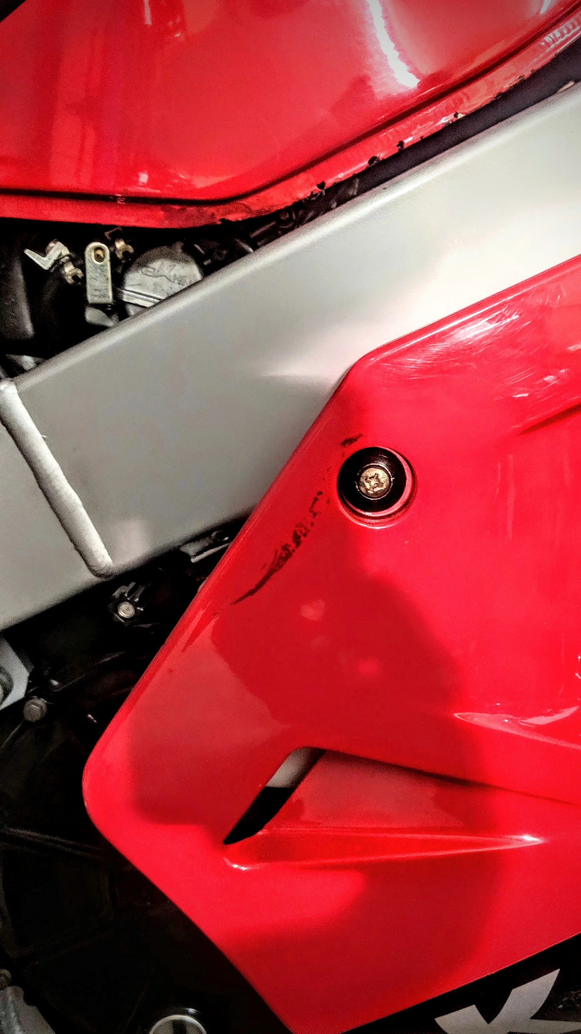 Close-up image of a red motorcycle fairing with a black scratch and a screw visible.