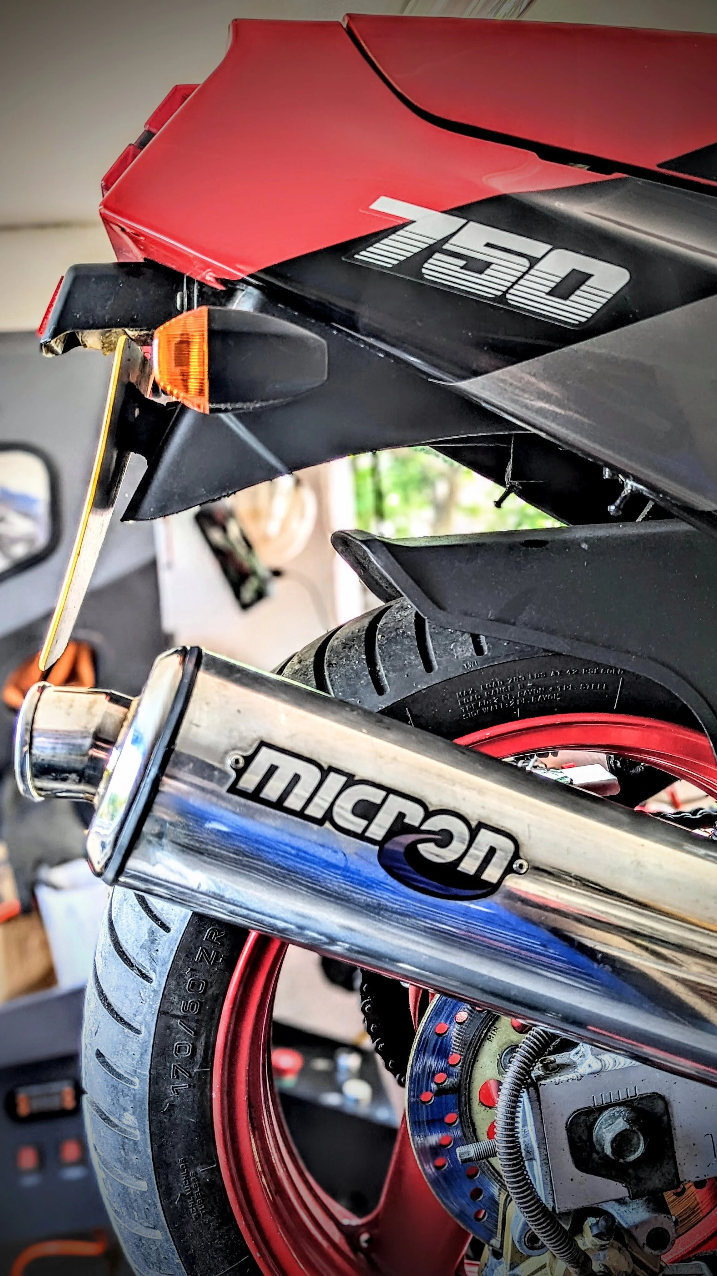 Close-up of a motorcycle showing the rear wheel, tire, and part of the exhaust pipe. The motorcycle has a red and black color scheme with a '150' decal on the body.