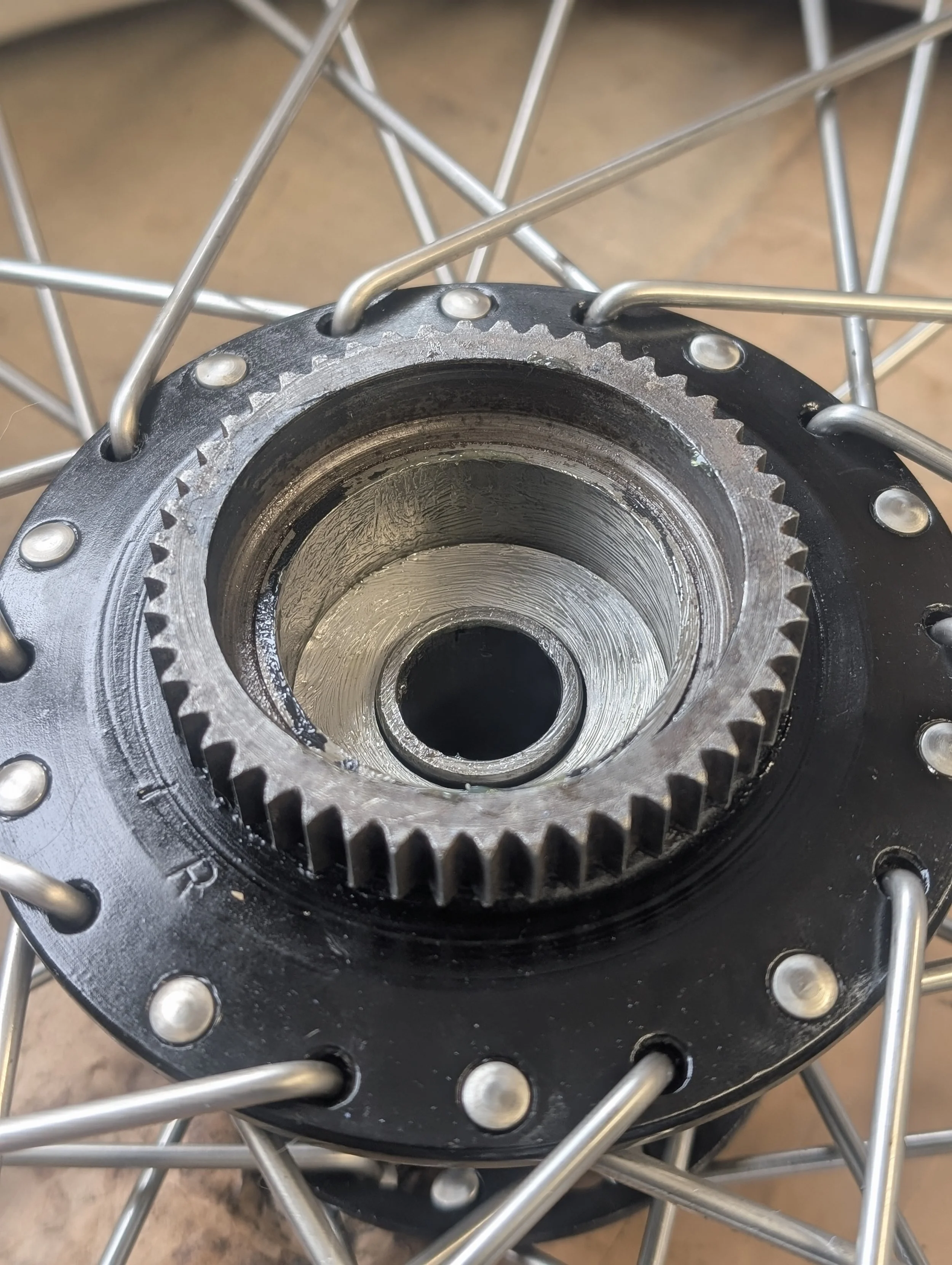 Close-up of a classic Triumph T100 QD Quick Disassembly rear wheel hub with spokes attached. Wheel hub has been vapour blasted and painted black. Spokes have been replaced with stainless steel as part of a barn find motorcycle 
restoration. 