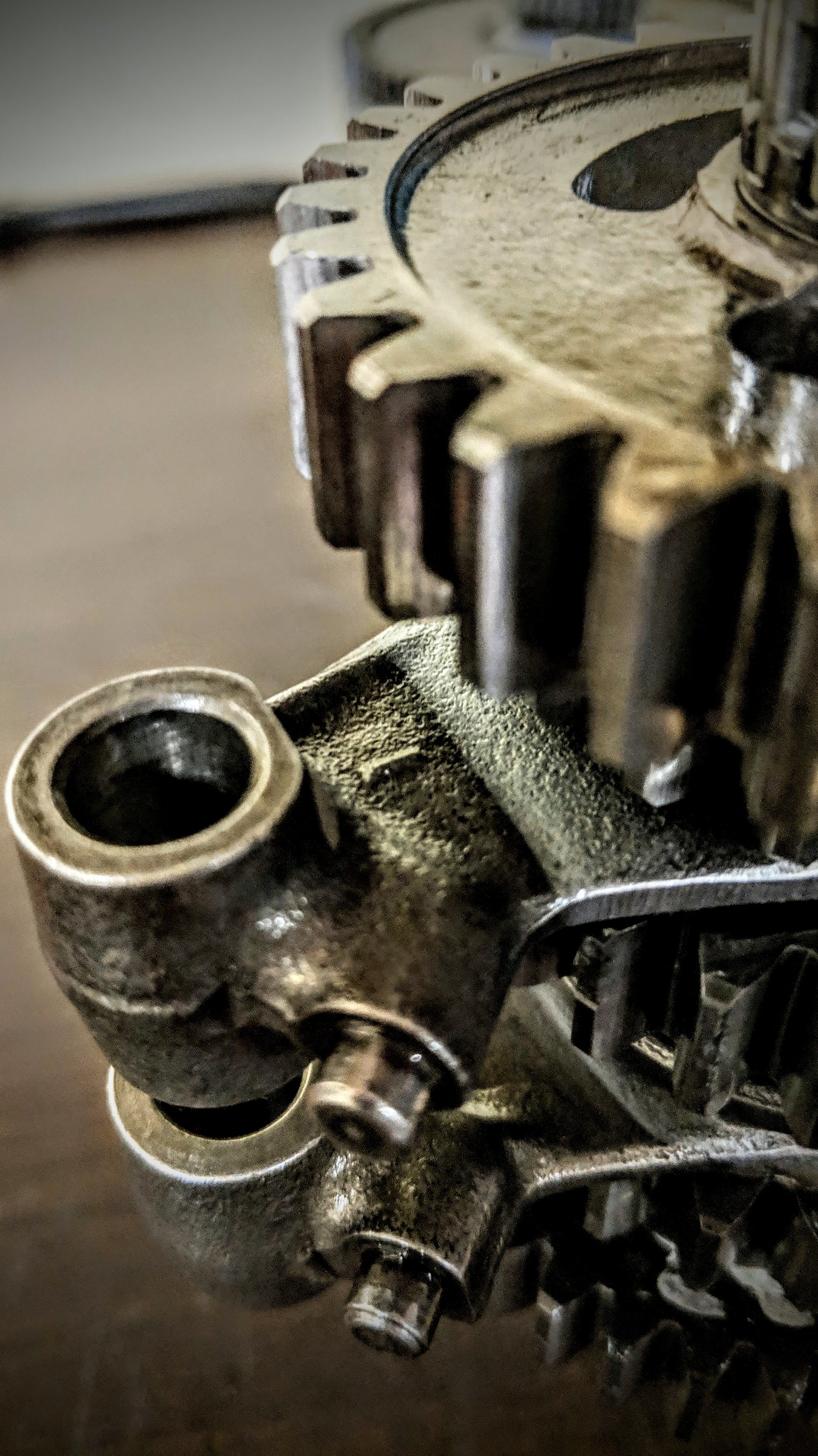 Close-up of a metallic mechanical component, possibly part of an engine or machinery, with visible gears, pipes, and textured surface.