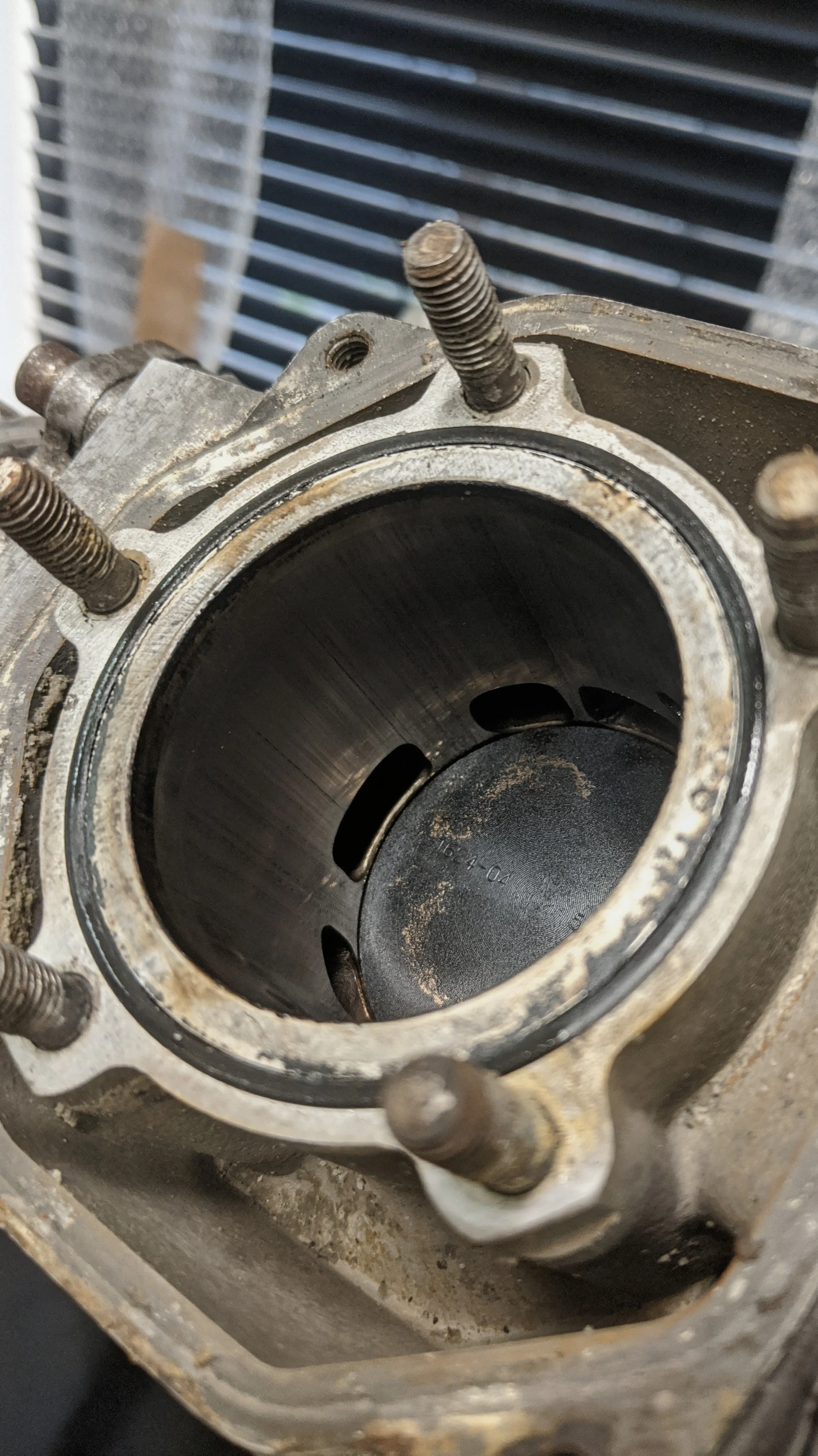 Close-up view of a car engine cylinder, showing the cylinder bore, piston, and surrounding engine block with visible bolts.