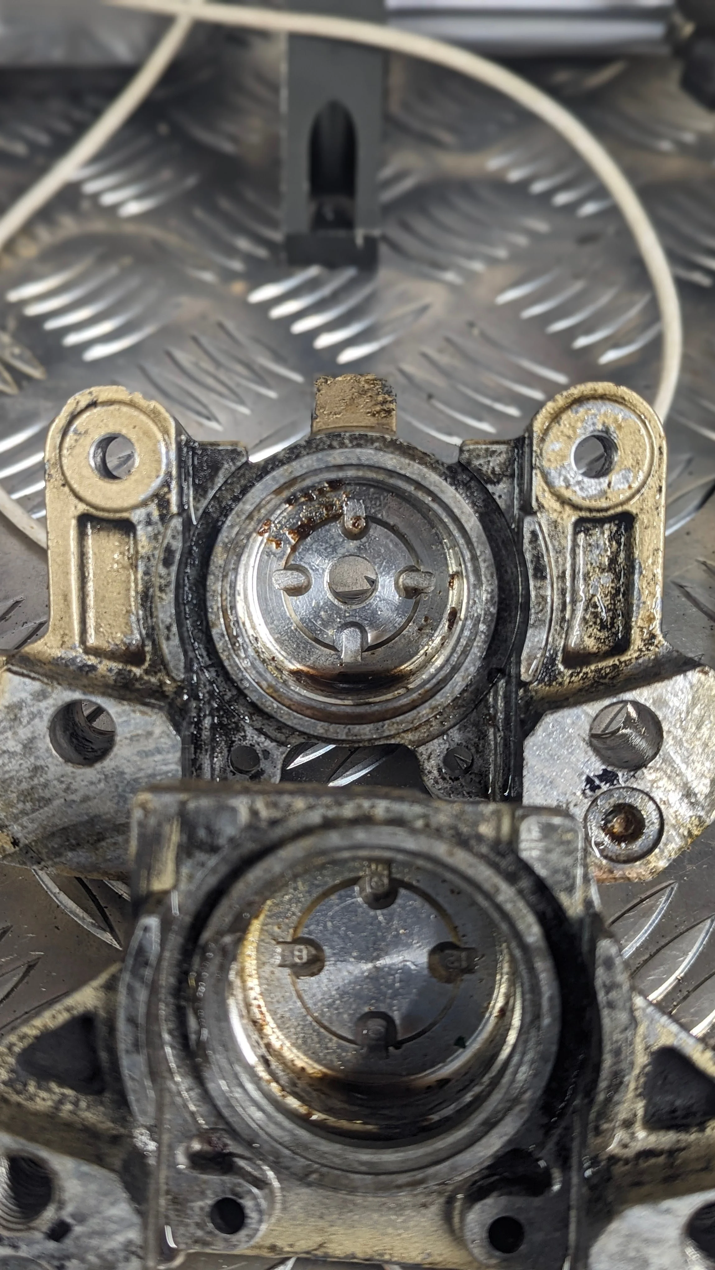 Close-up of mechanical engine parts, appearing worn and dirty, with visible metal components and bolt holes.