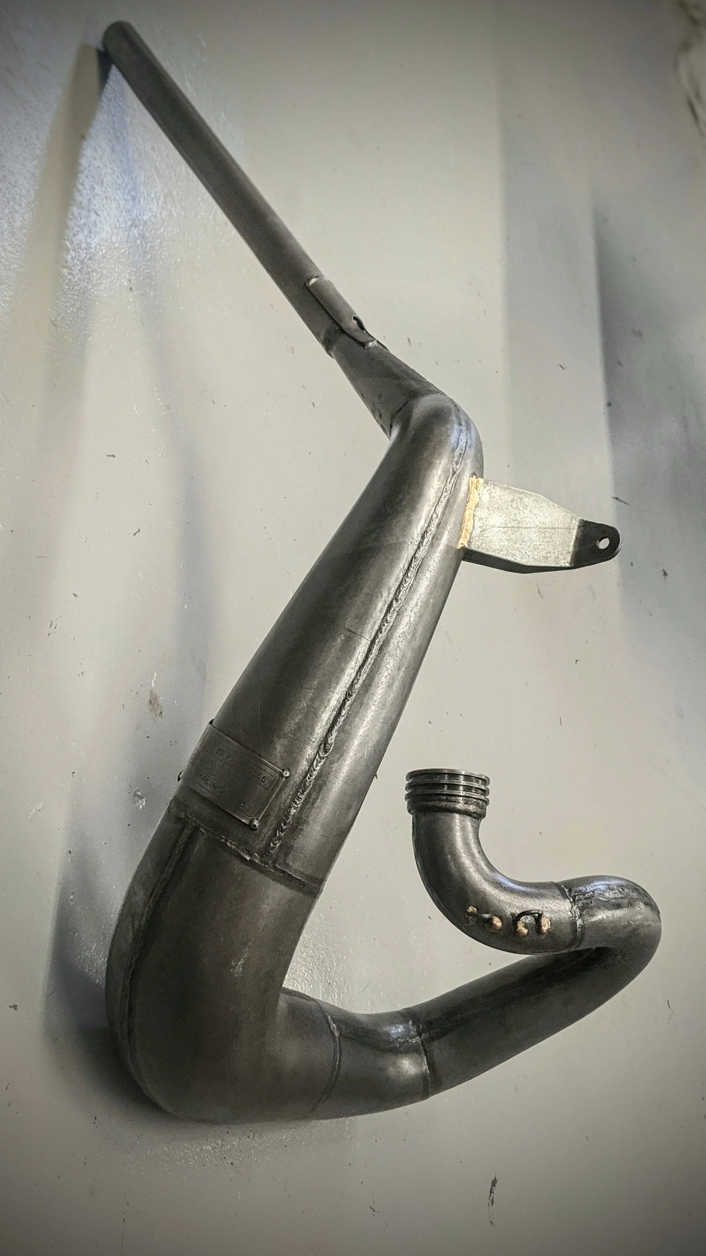 A metallic exhaust pipe with a bent pipe section, mounted on a wall.
