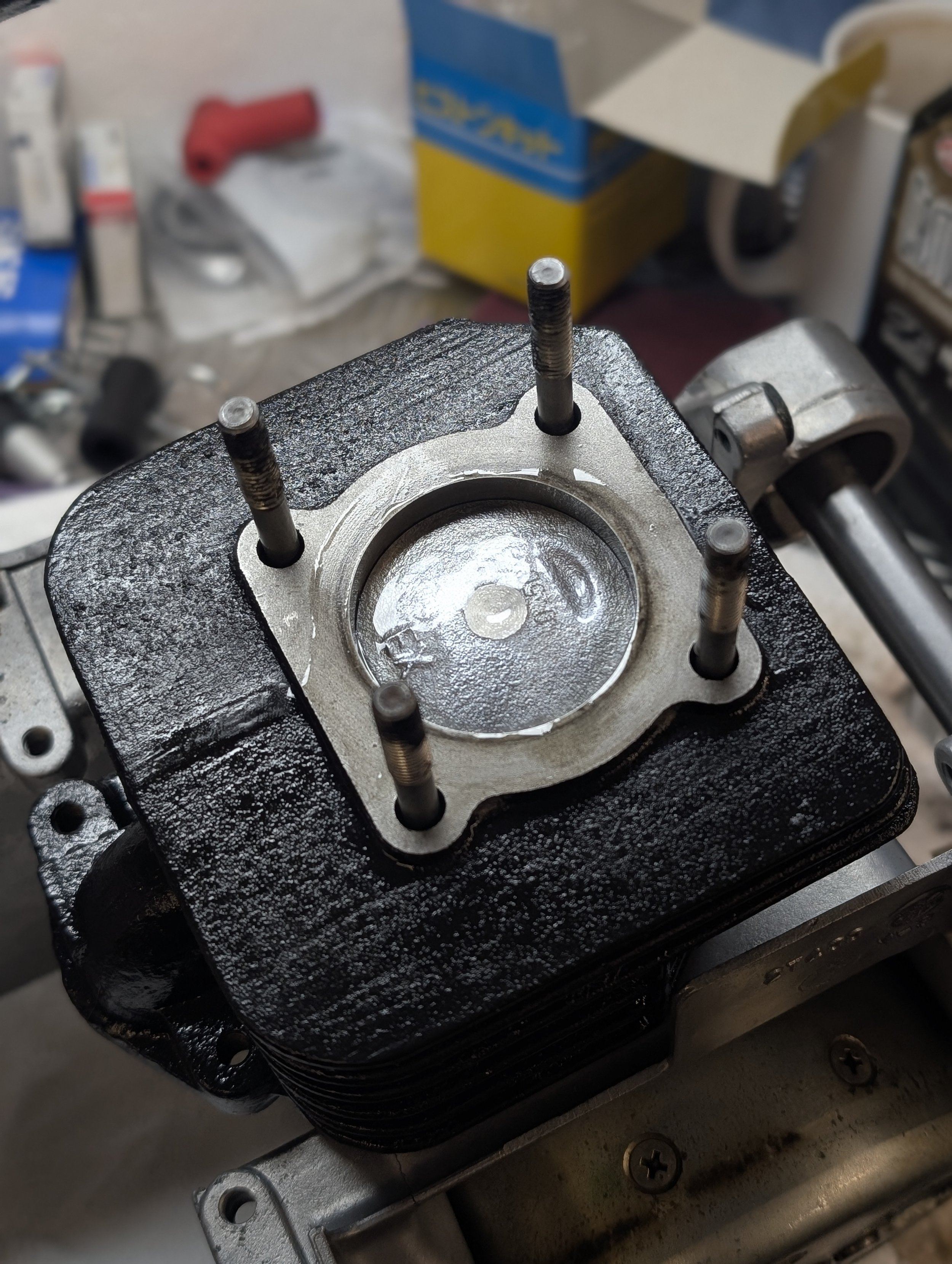 Close-up of a disassembled engine cylinder head with visible valve stems, set on a workbench with tools and parts in the background.