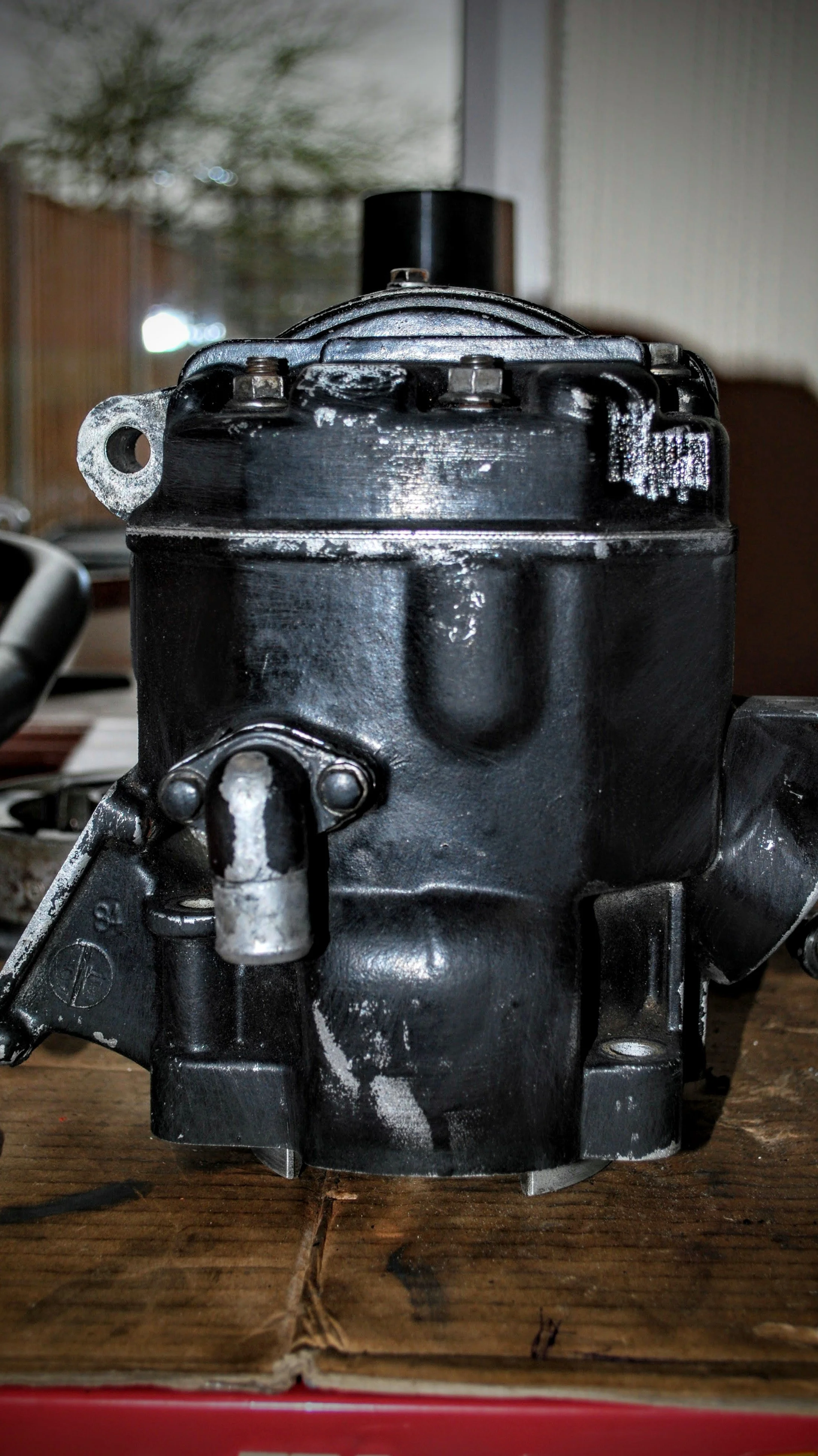 A black car engine component on a wooden workbench with a blurred background.