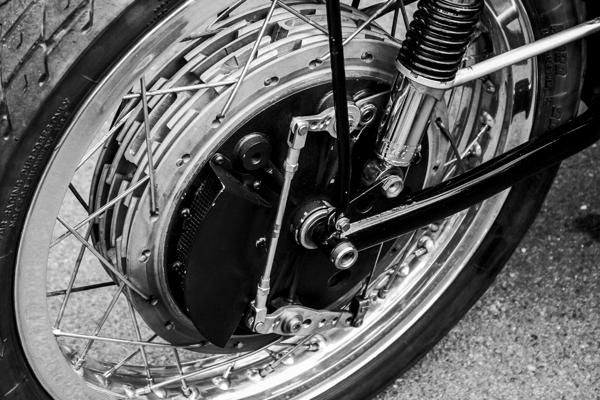 Close-up of a vintage motorcycle wheel showing spokes, brake disc, and suspension system in black and white.
