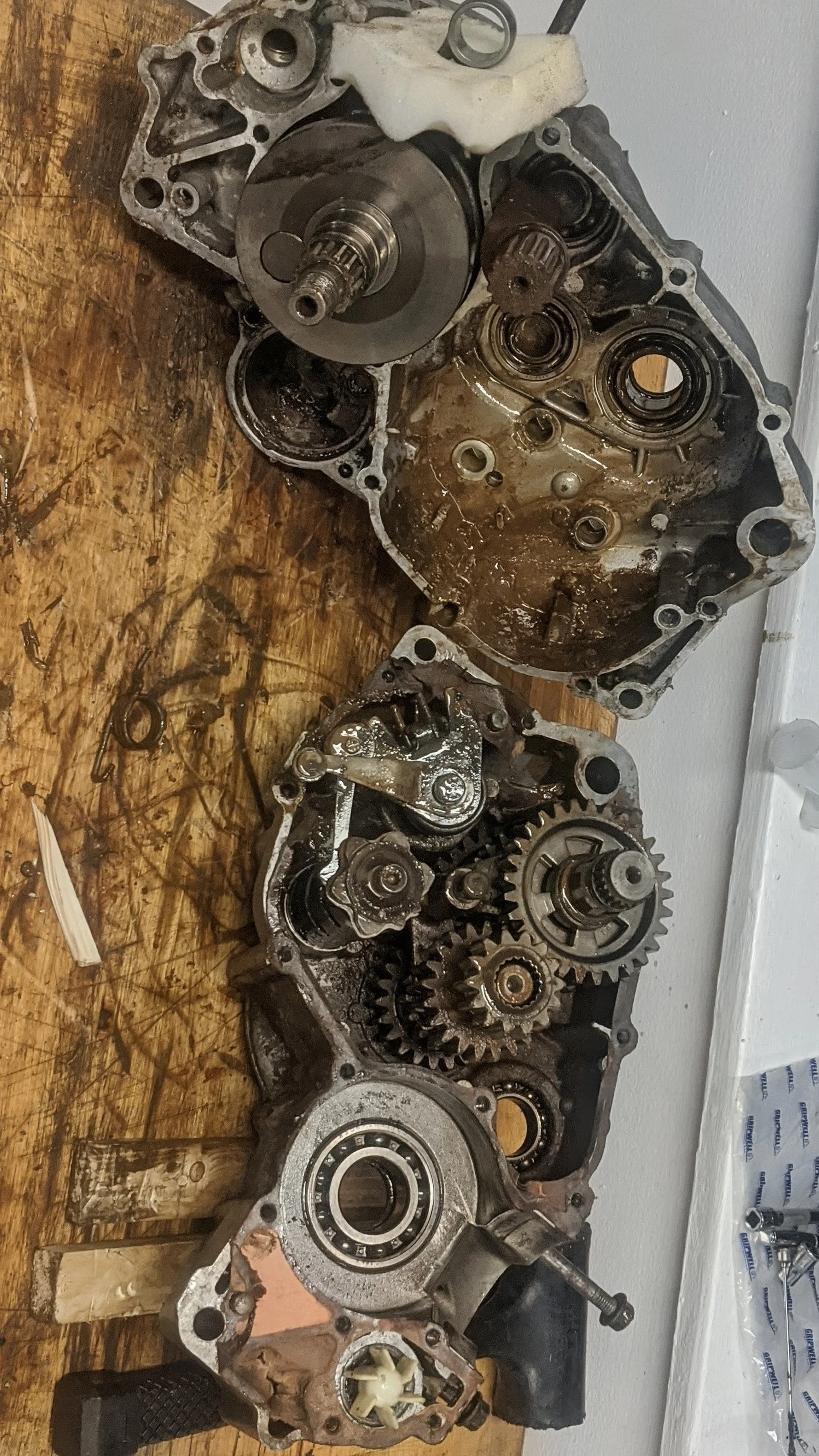 Disassembled automotive engine parts laid out on a wooden workbench, including gears, shafts, and engine casing.