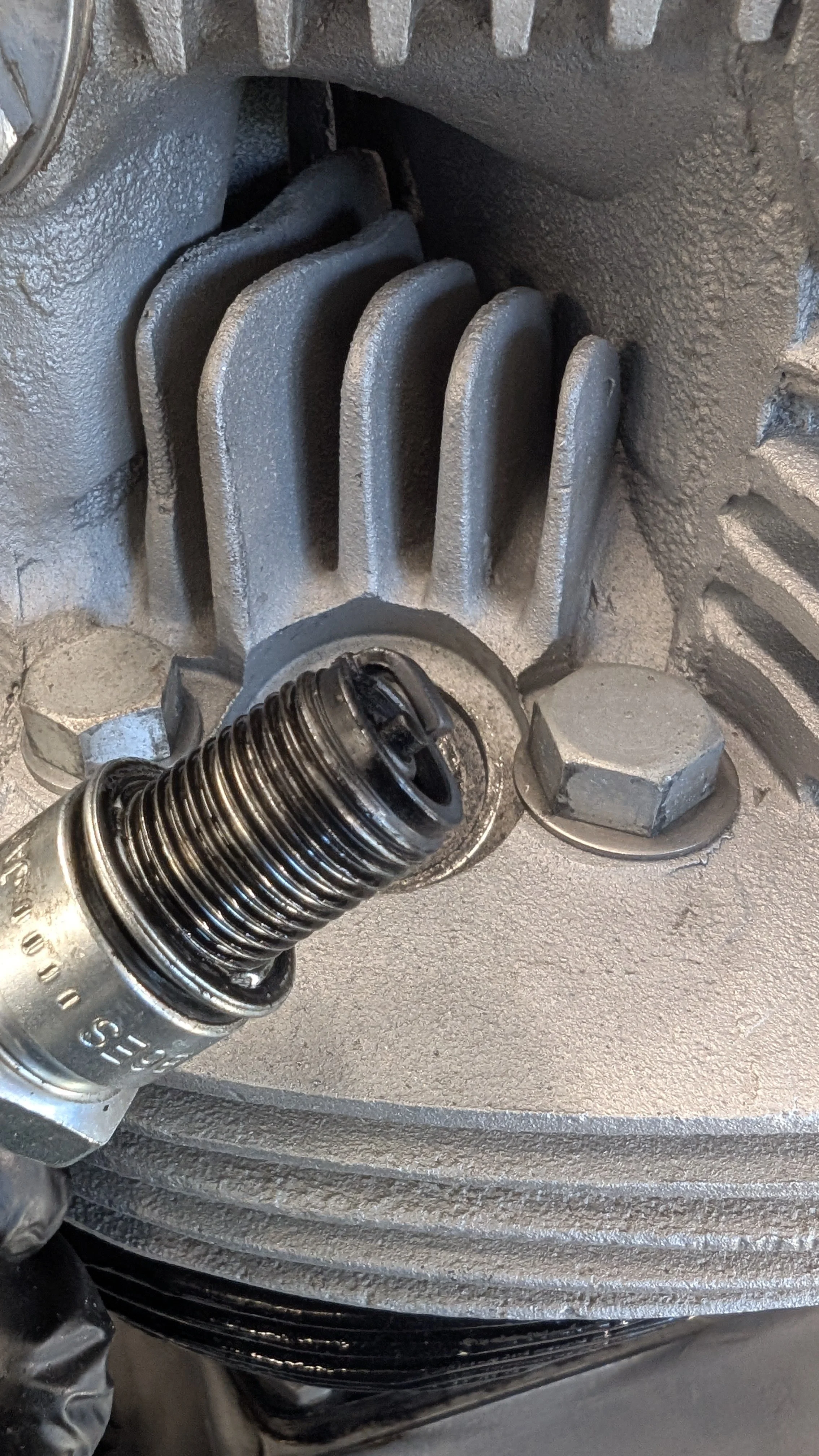 Close-up of a spark plug installed in an engine with visible cooling fins and bolts.