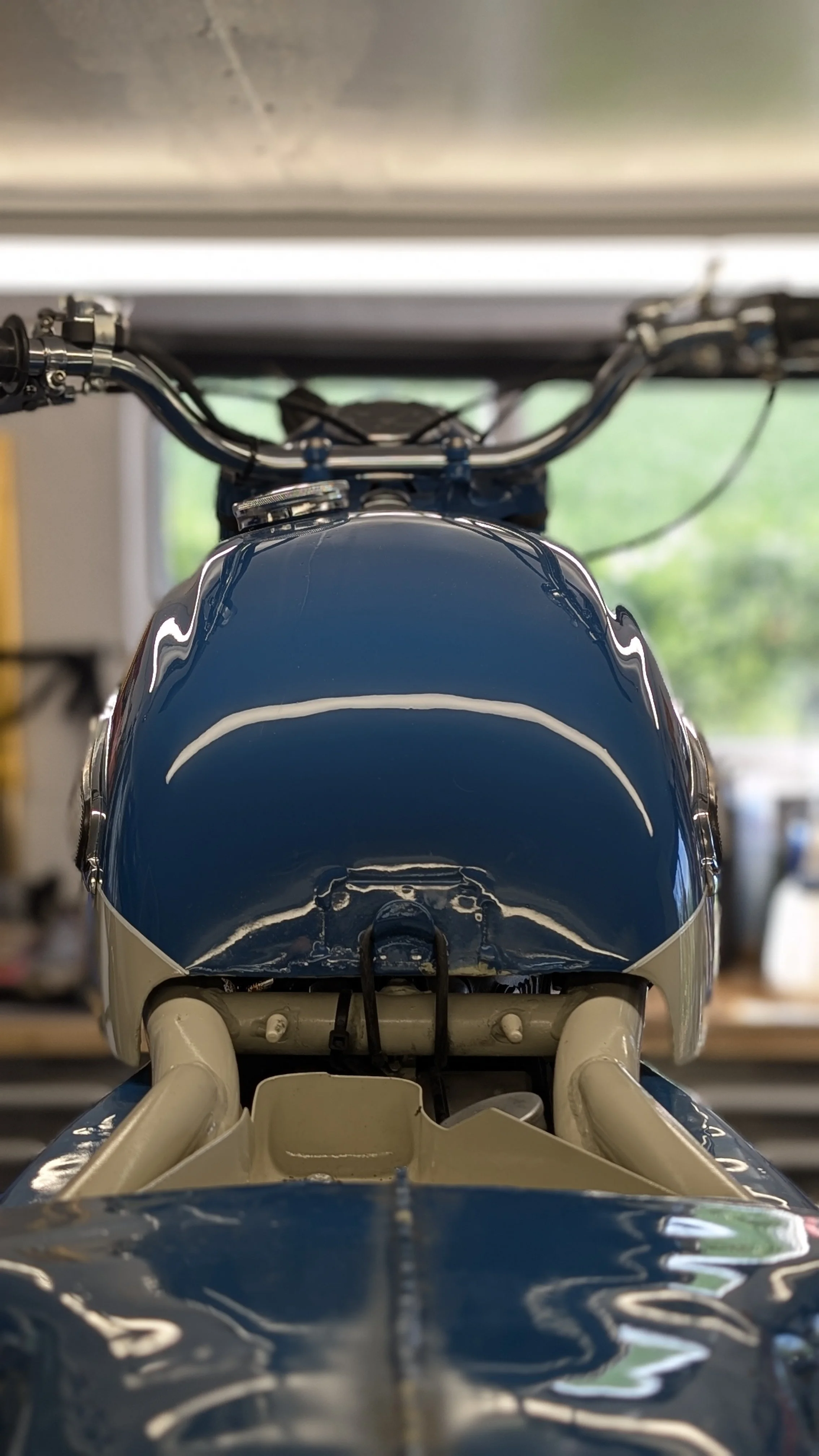Top-down view of a blue and white motorcycle inside a garage, with a blurred background showing the garage interior.