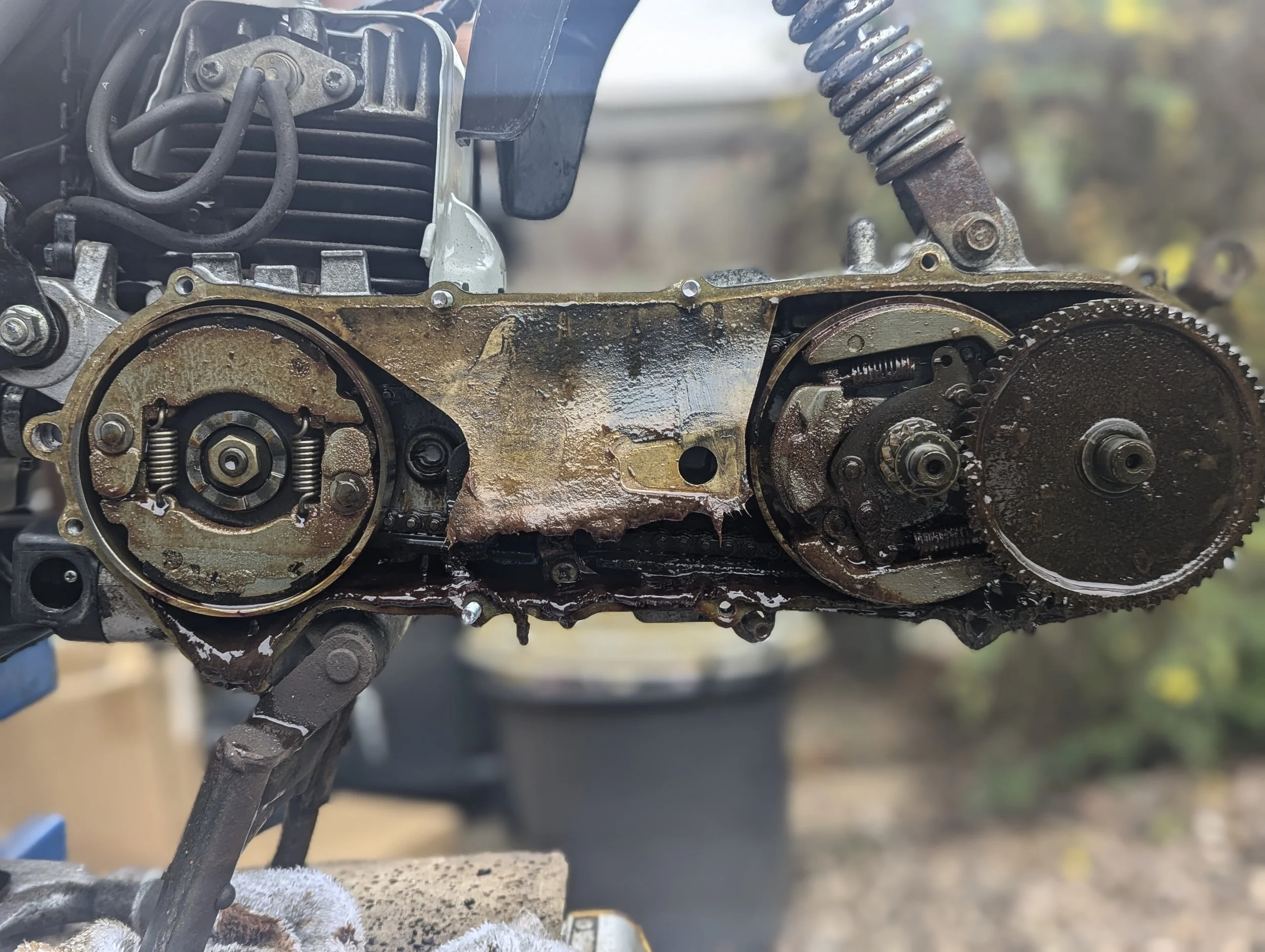 Close-up of the internal parts of a motorcycle engine, showing rusted gears, chains, and metal components with dirt and oil.