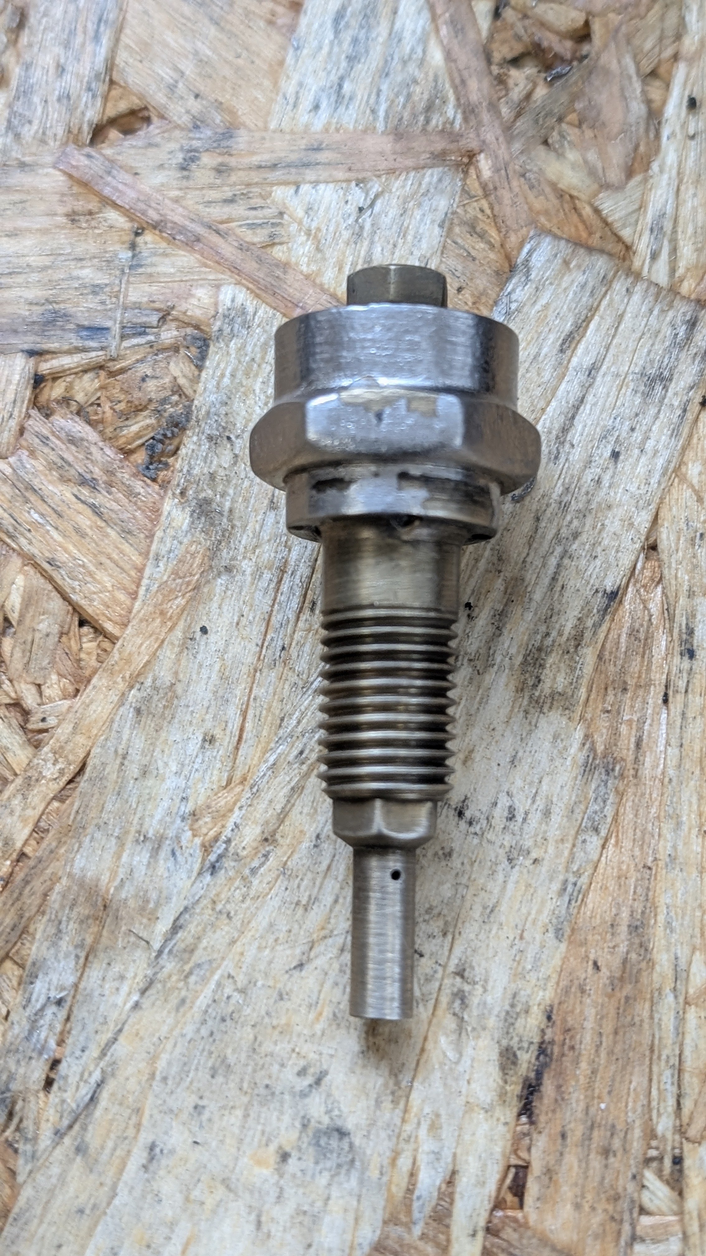 A metal bolt with a hexagonal head and a threaded shaft resting on a wooden surface.