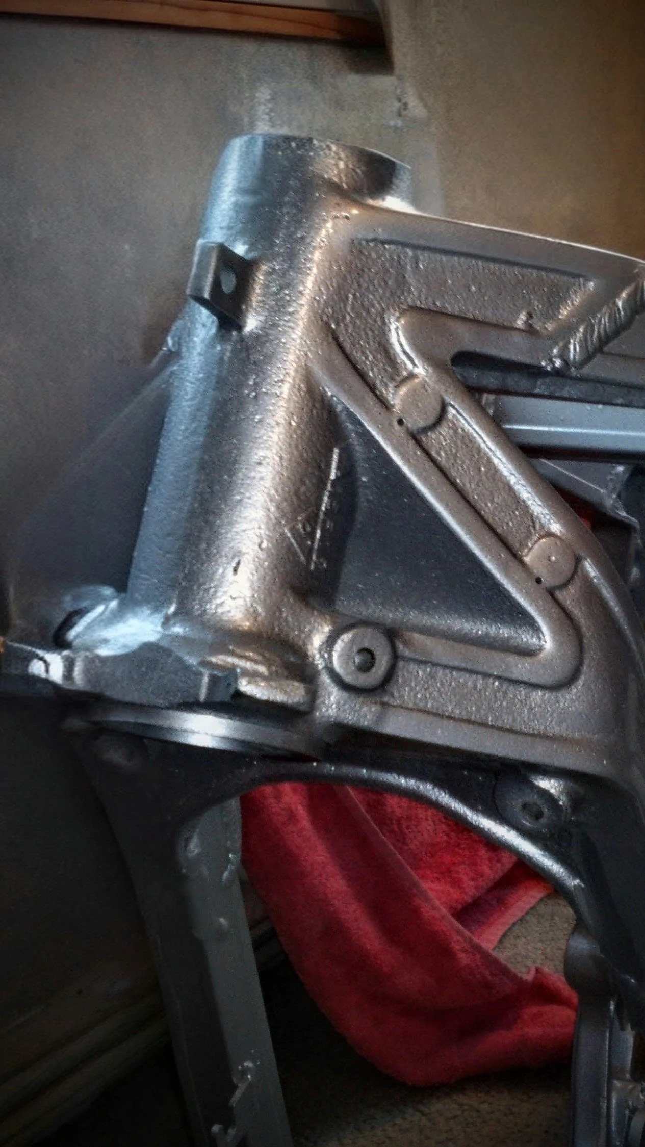 Close-up of a metallic mechanical device, possibly part of machinery or equipment, with a textured surface and structural components, placed over a piece of red fabric.