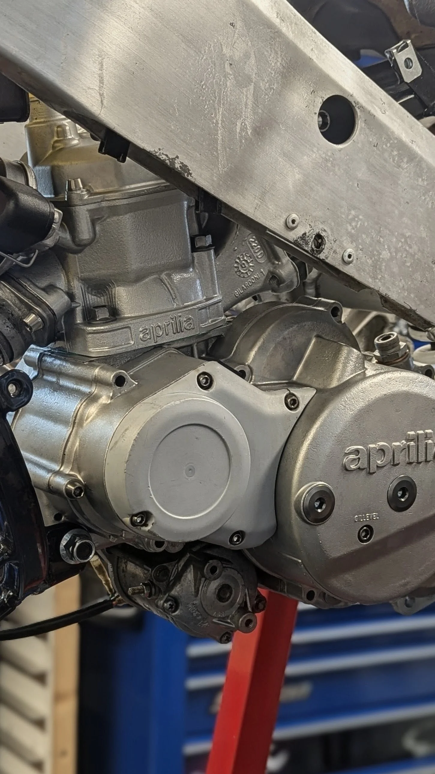 Close-up of an Aprilia motorcycle engine with a metal support beam in the background.