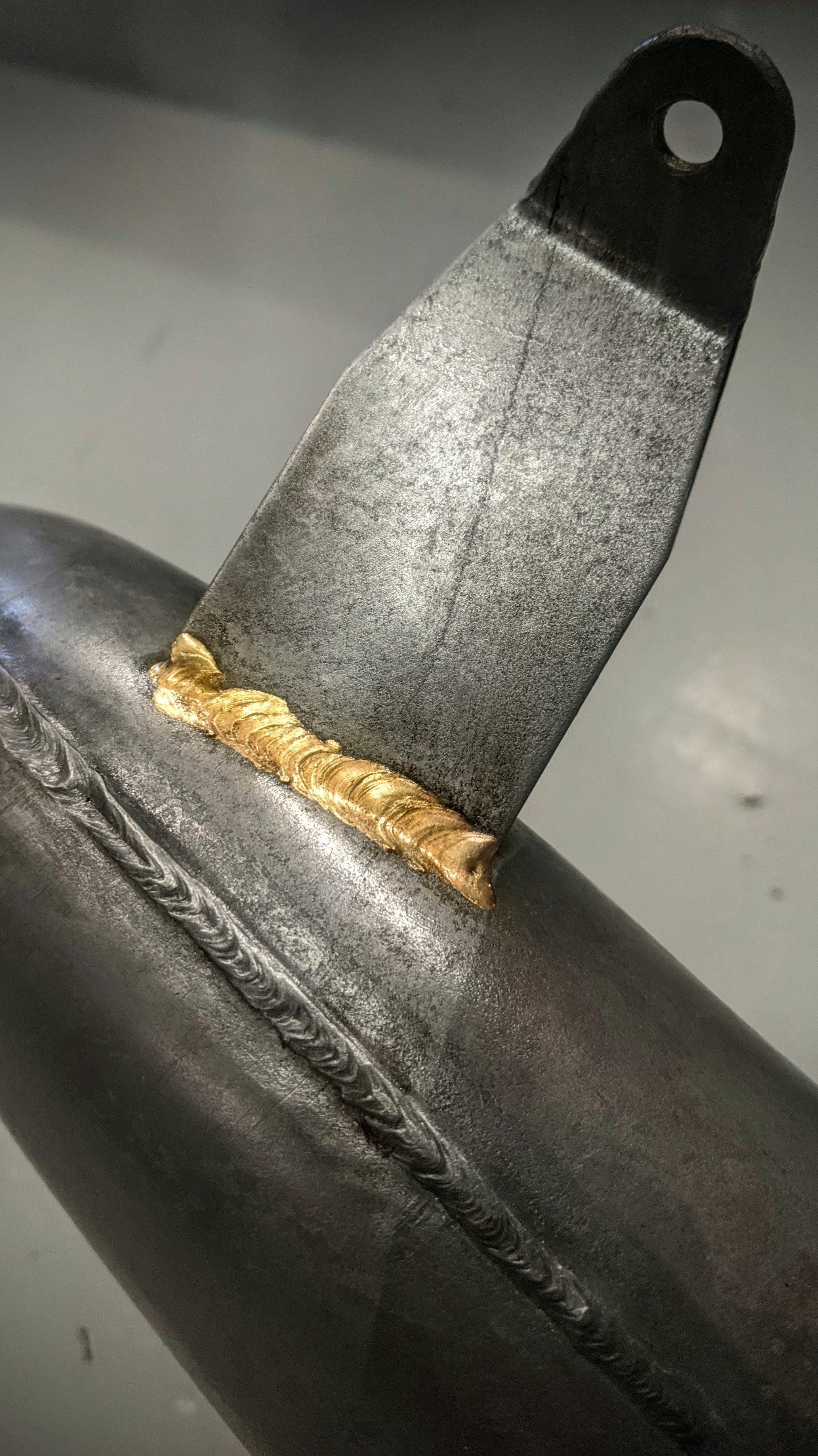 Close-up of a metal weld joint with a gold-colored weld bead on a steel component.