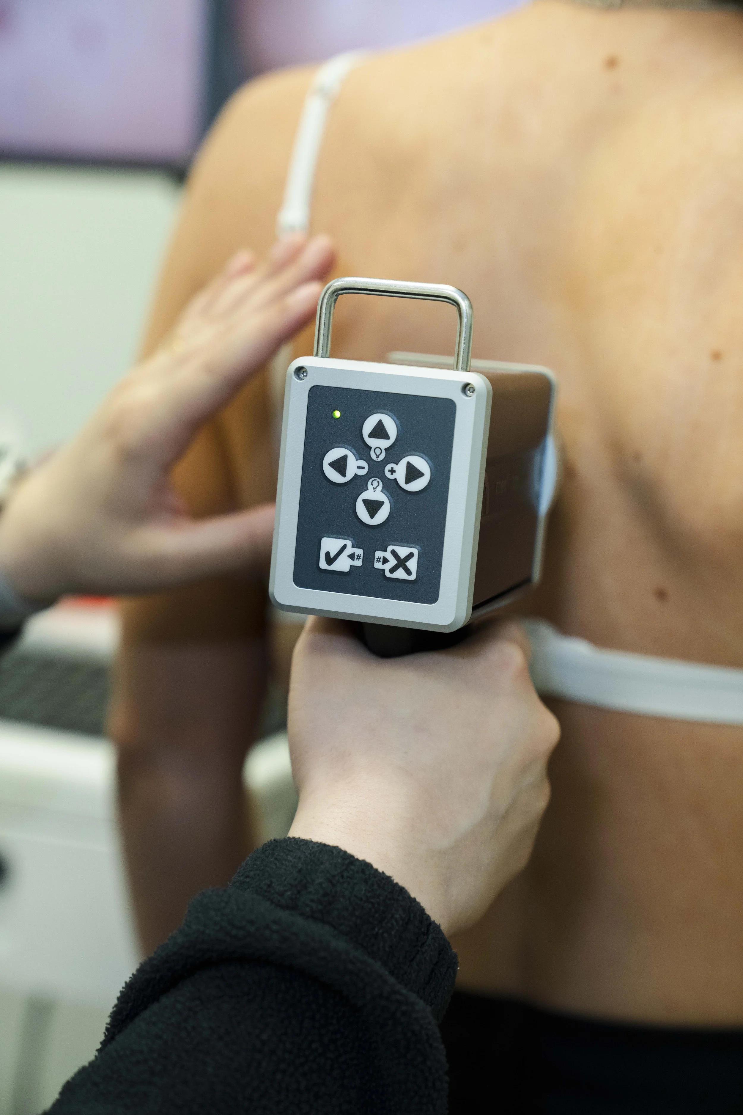 Close-up of a infrared thermometer pointing at the shoulder of a person with a lightning bolt tattoo on their shoulder, in a medical setting.