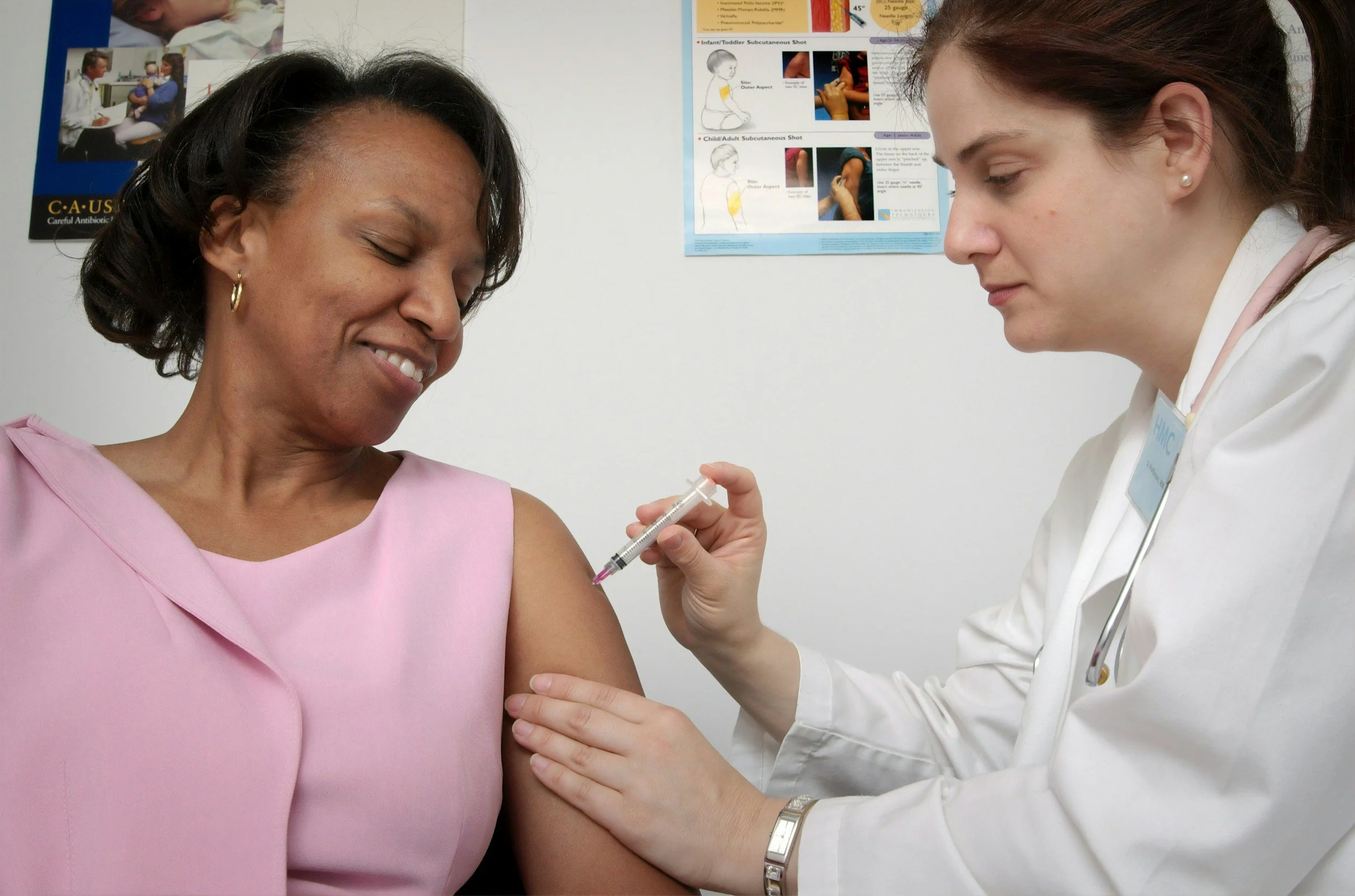 A woman in pink scrubs receiving a vaccination from a healthcare professional in a white coat.