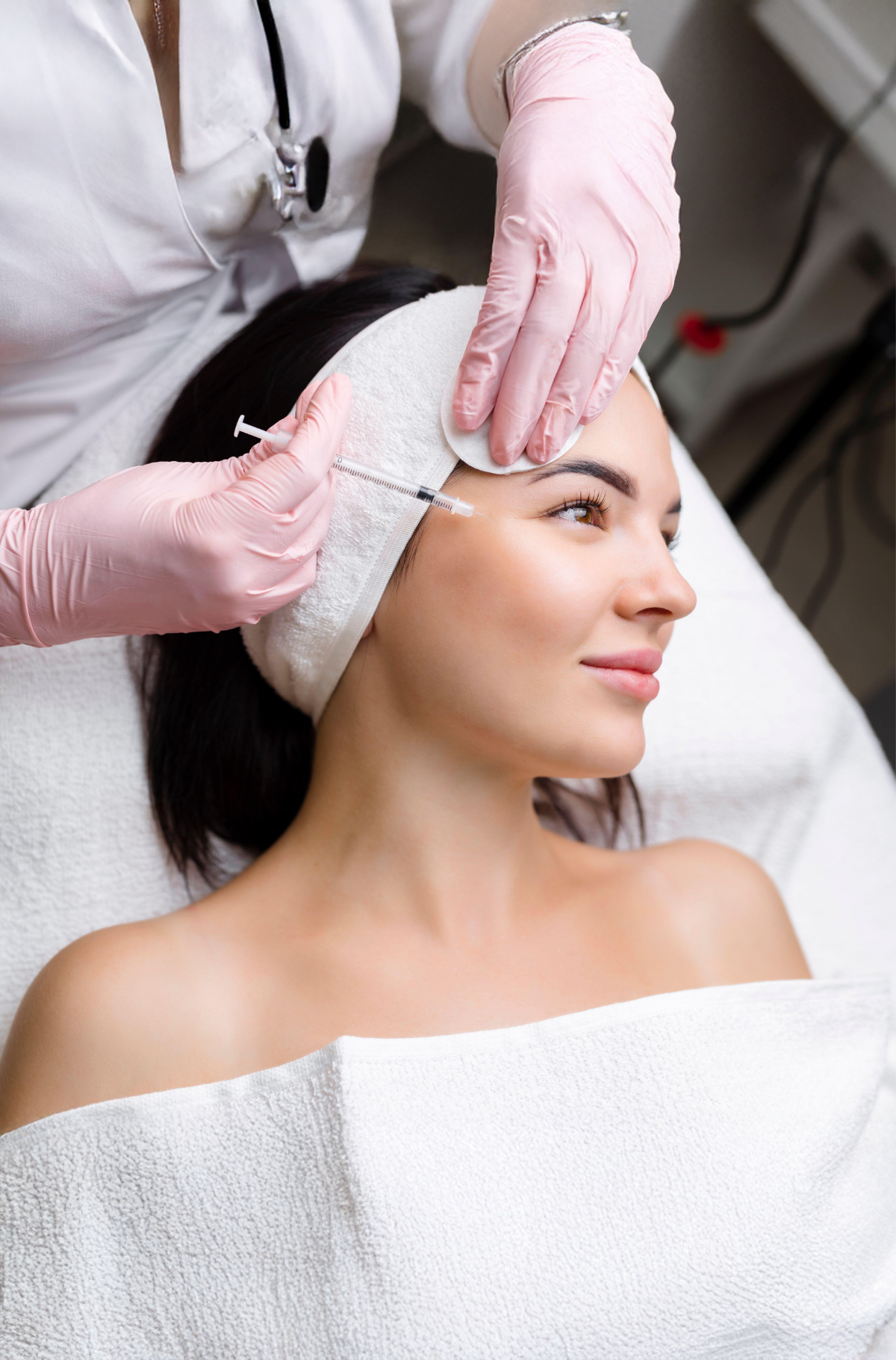A woman receiving a Botox injection in her forehead from a healthcare professional wearing pink gloves in a clinical setting.