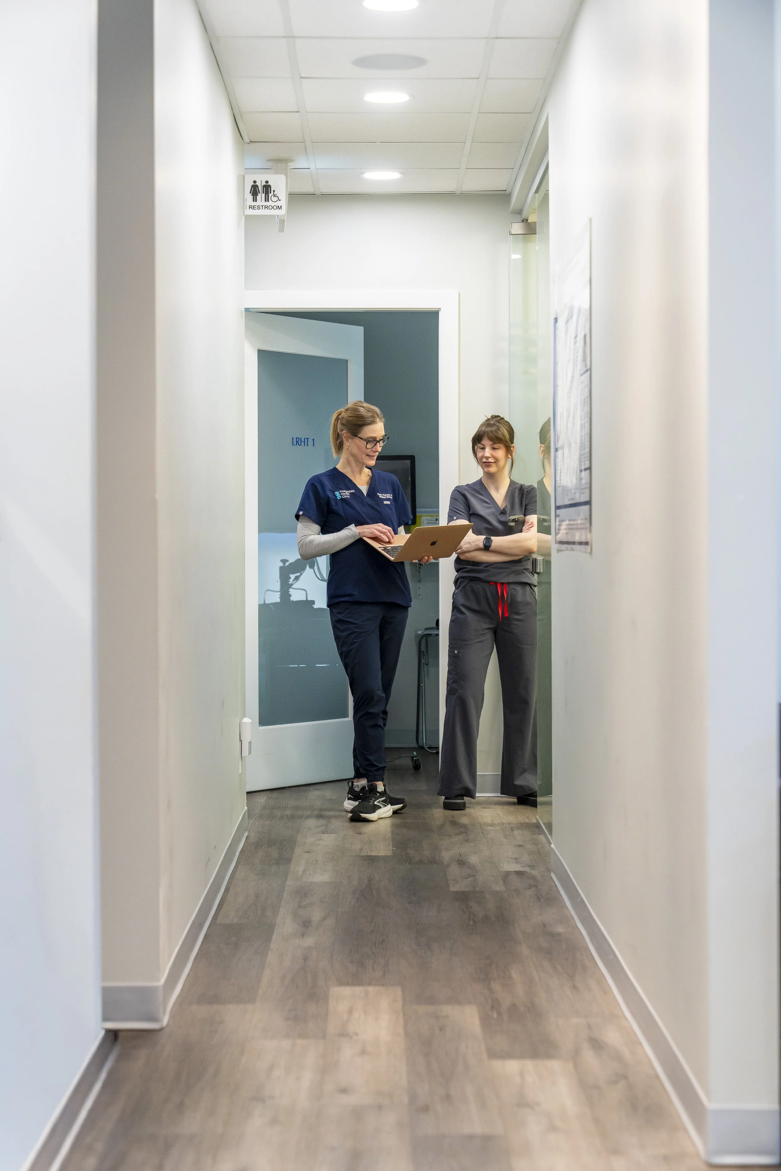 Two healthcare workers standing in a hospital corridor, looking at a tablet.