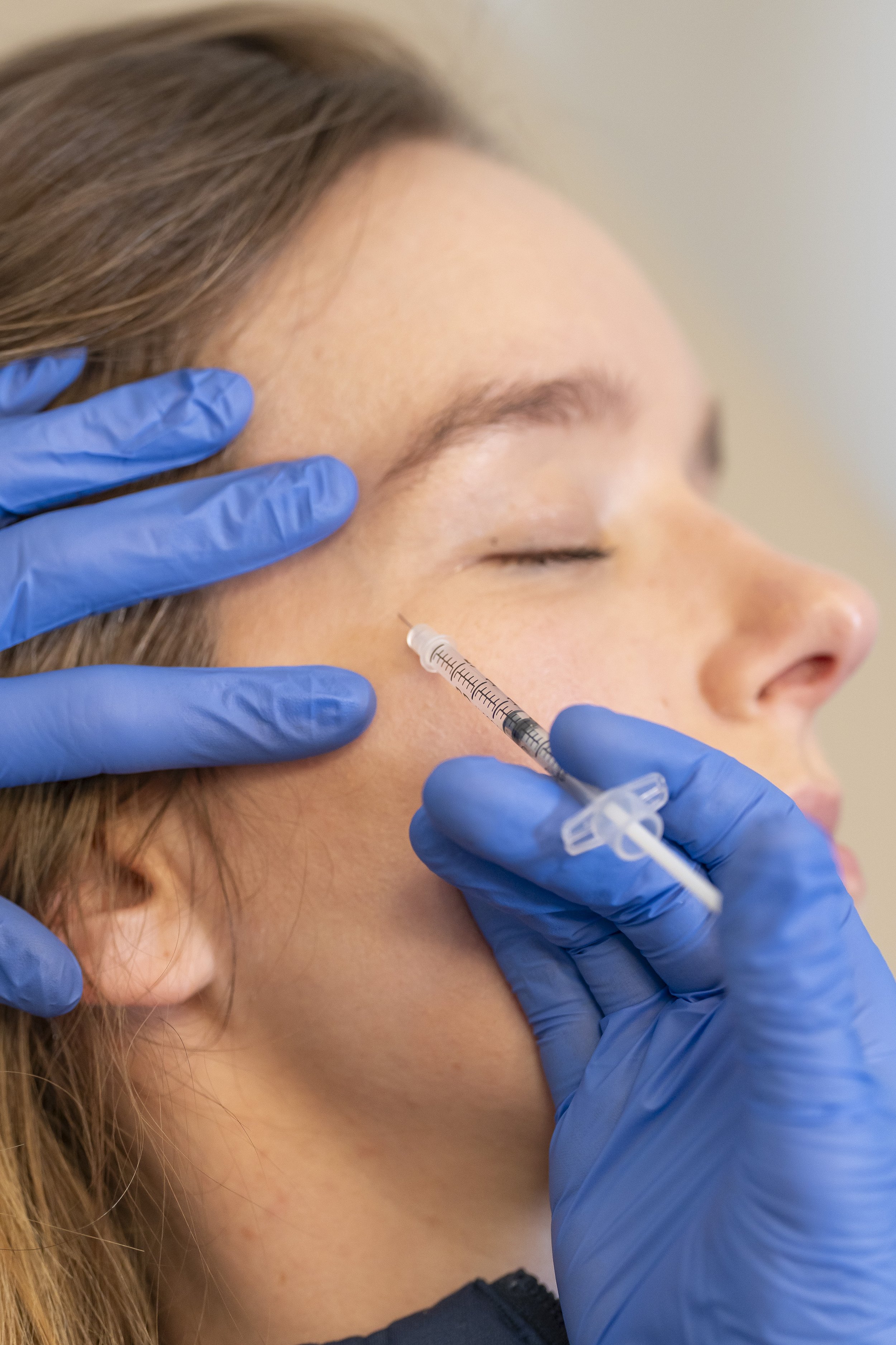 A person with long hair receiving an injection in their face from a healthcare professional wearing blue gloves.