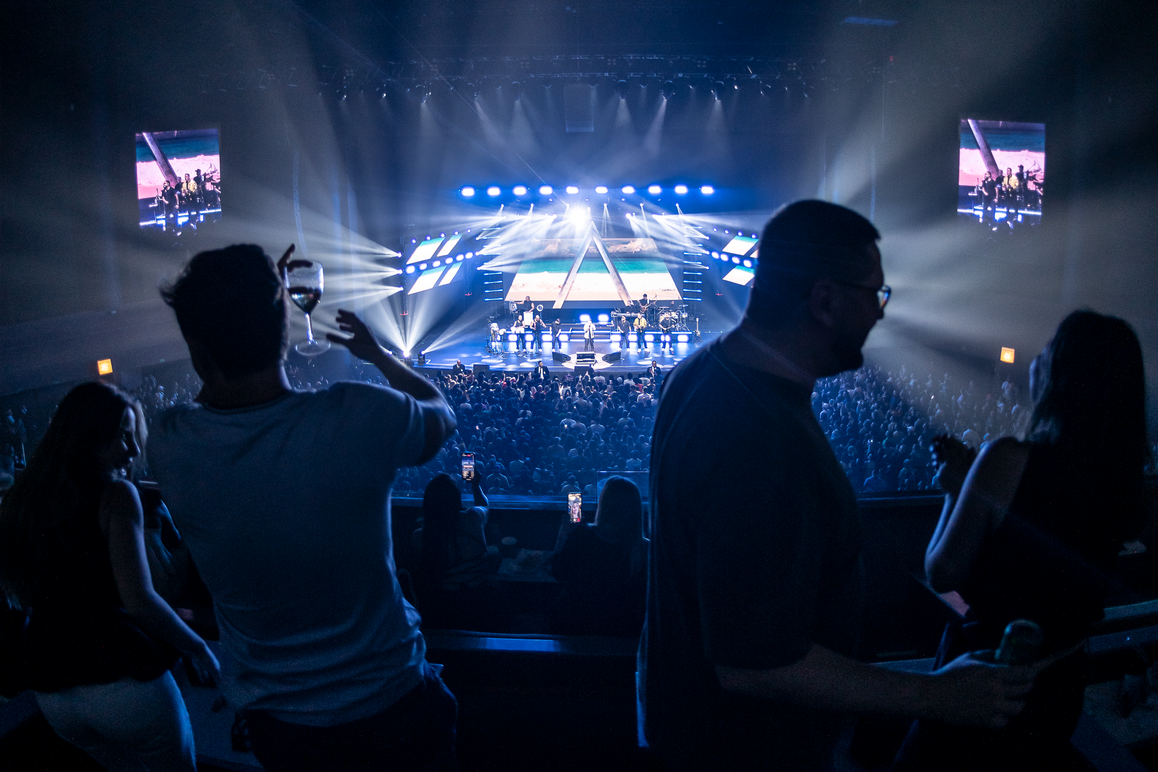 Pessoa registra pelo celular um show com palco iluminado e público ao fundo