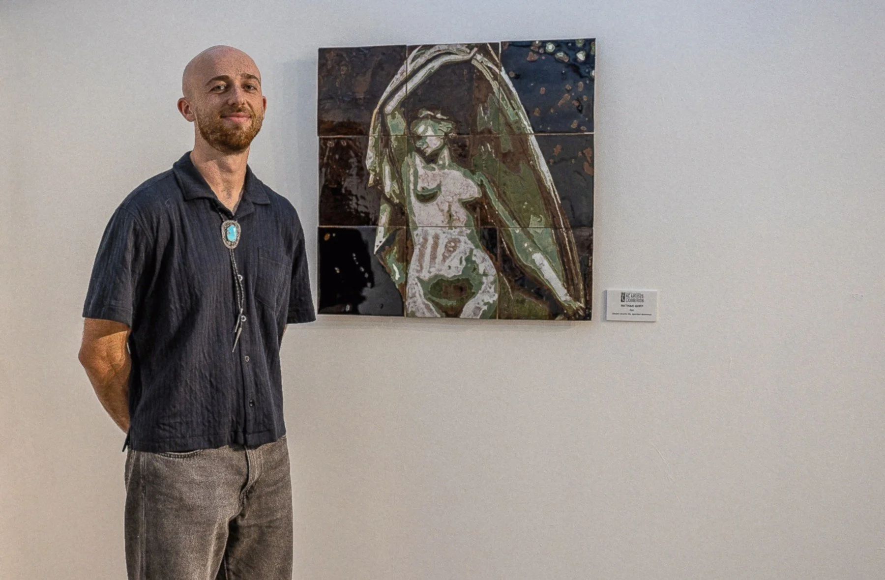 A man standing next to a multi-panel artwork depicting a stylized face of the Virgin Mary on a white gallery wall.
