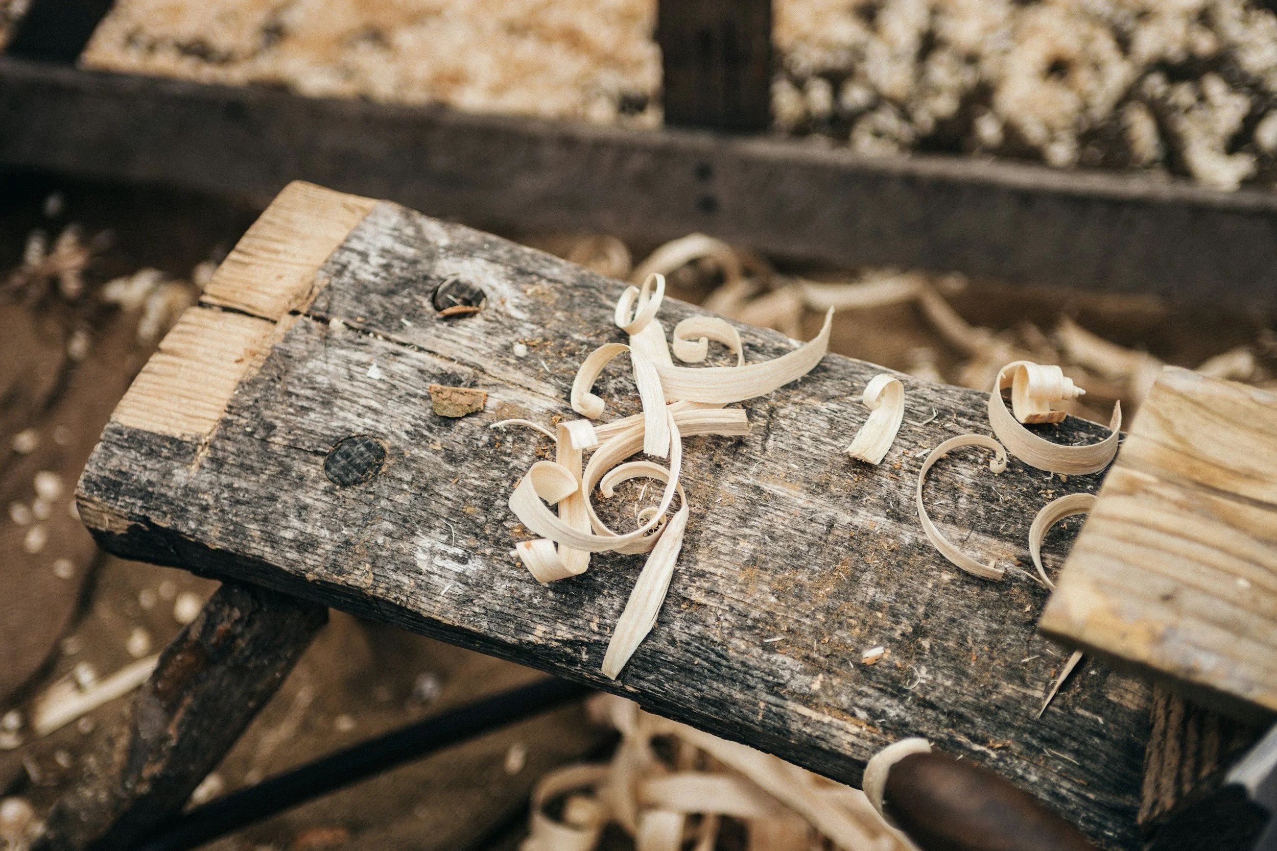 Close-up of wood shavings on a rustic wooden workbench in a woodworking shop.