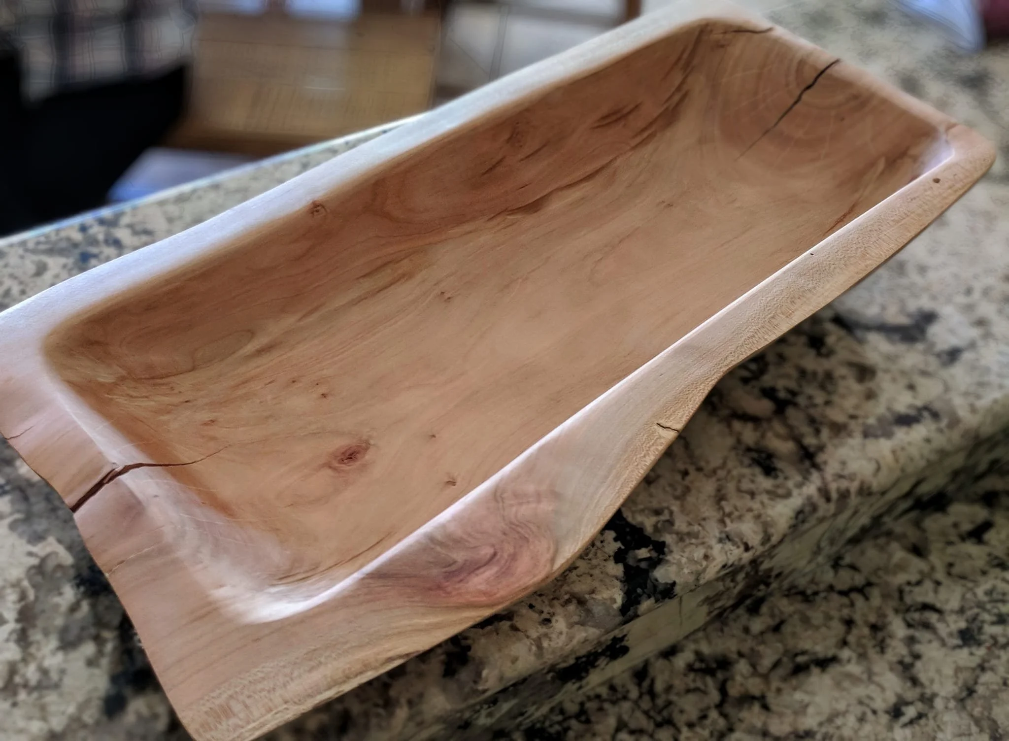 A wooden bowl with a natural grain pattern, placed on a granite countertop.