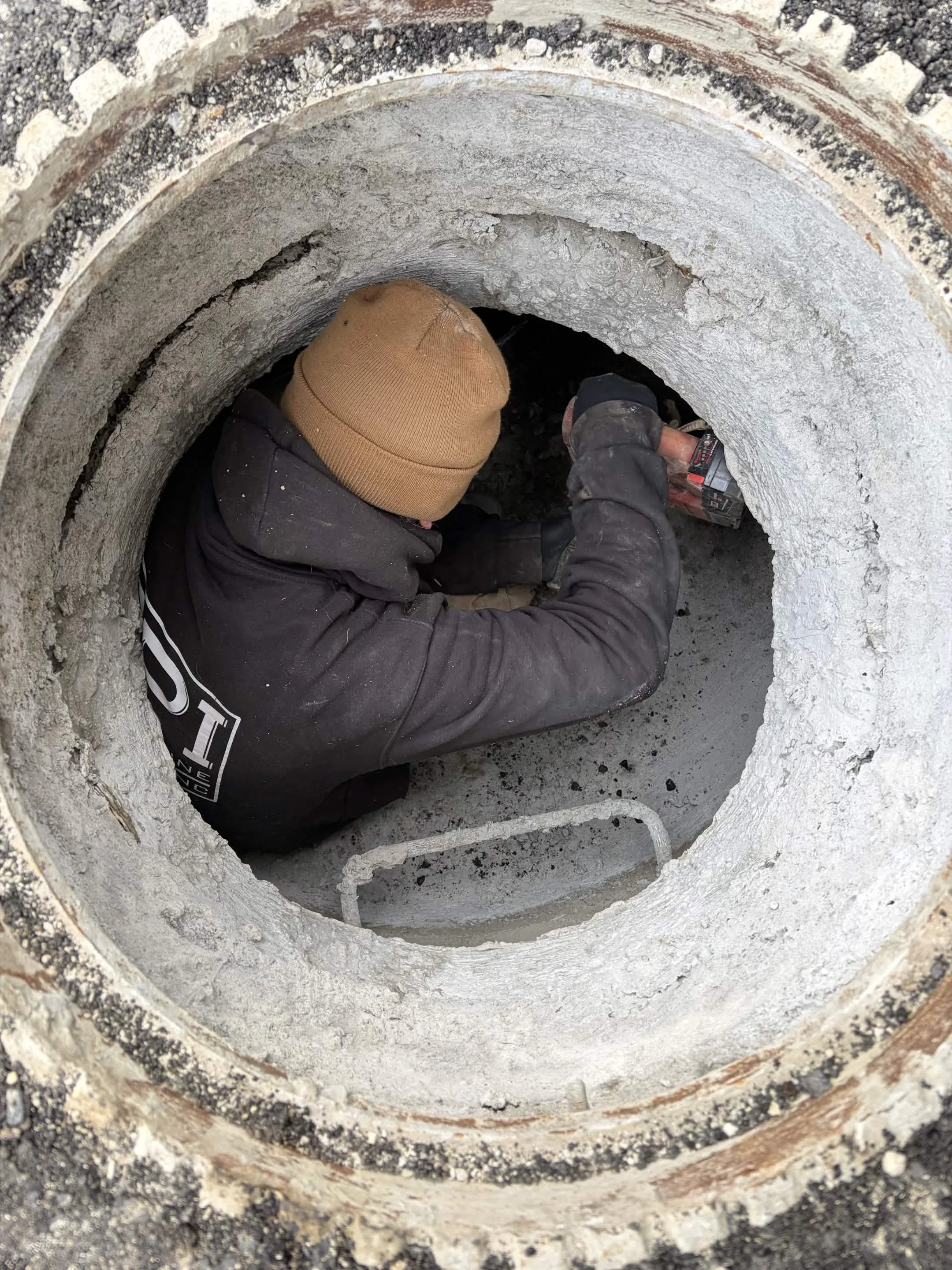 Worker using a power drill inside a large concrete pipe.