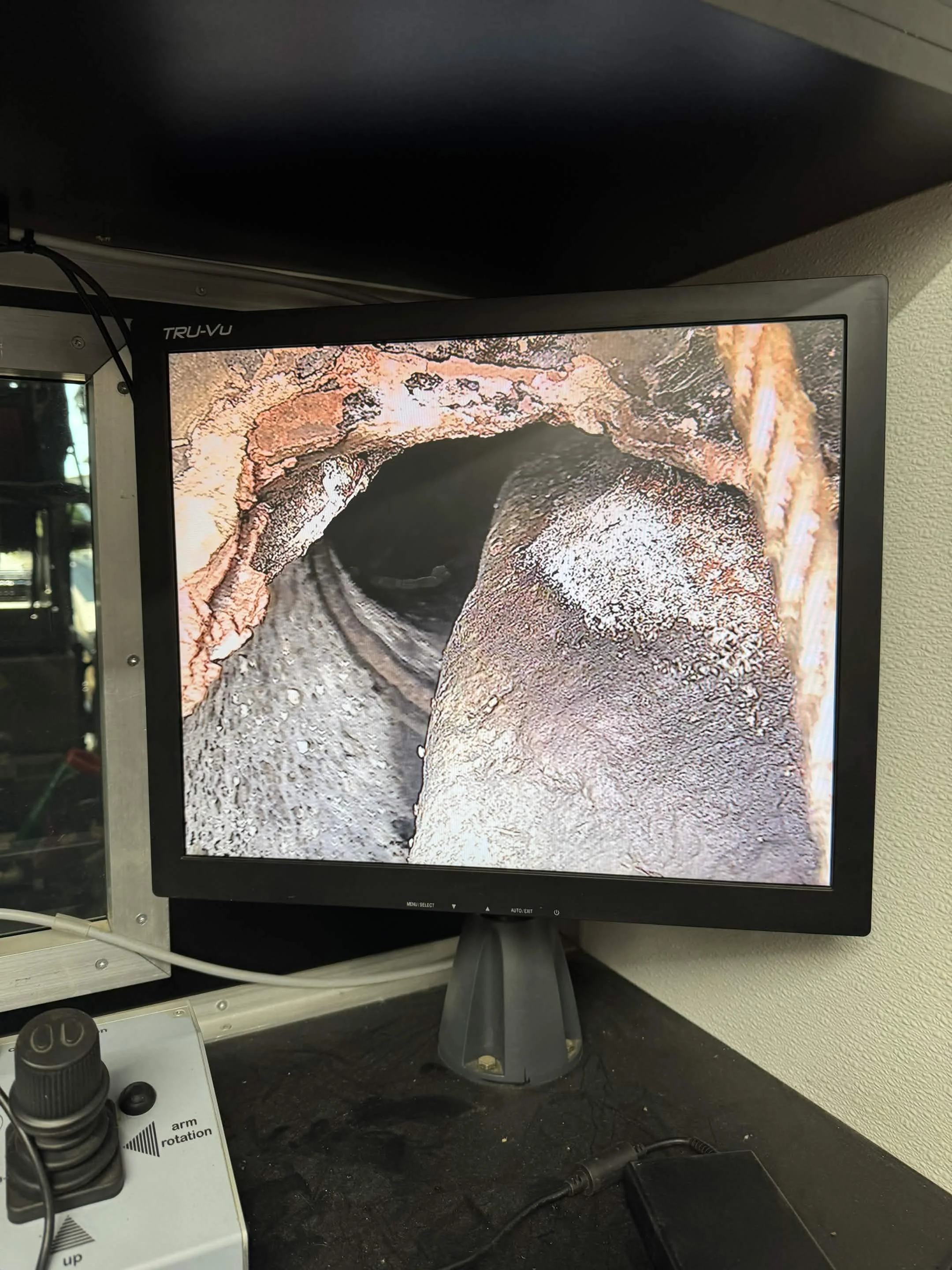 Close-up of a computer monitor displaying a geological or archaeological image of a rock formation or excavation site, with a small part of the black desk, a joystick, and some cables visible in the foreground.