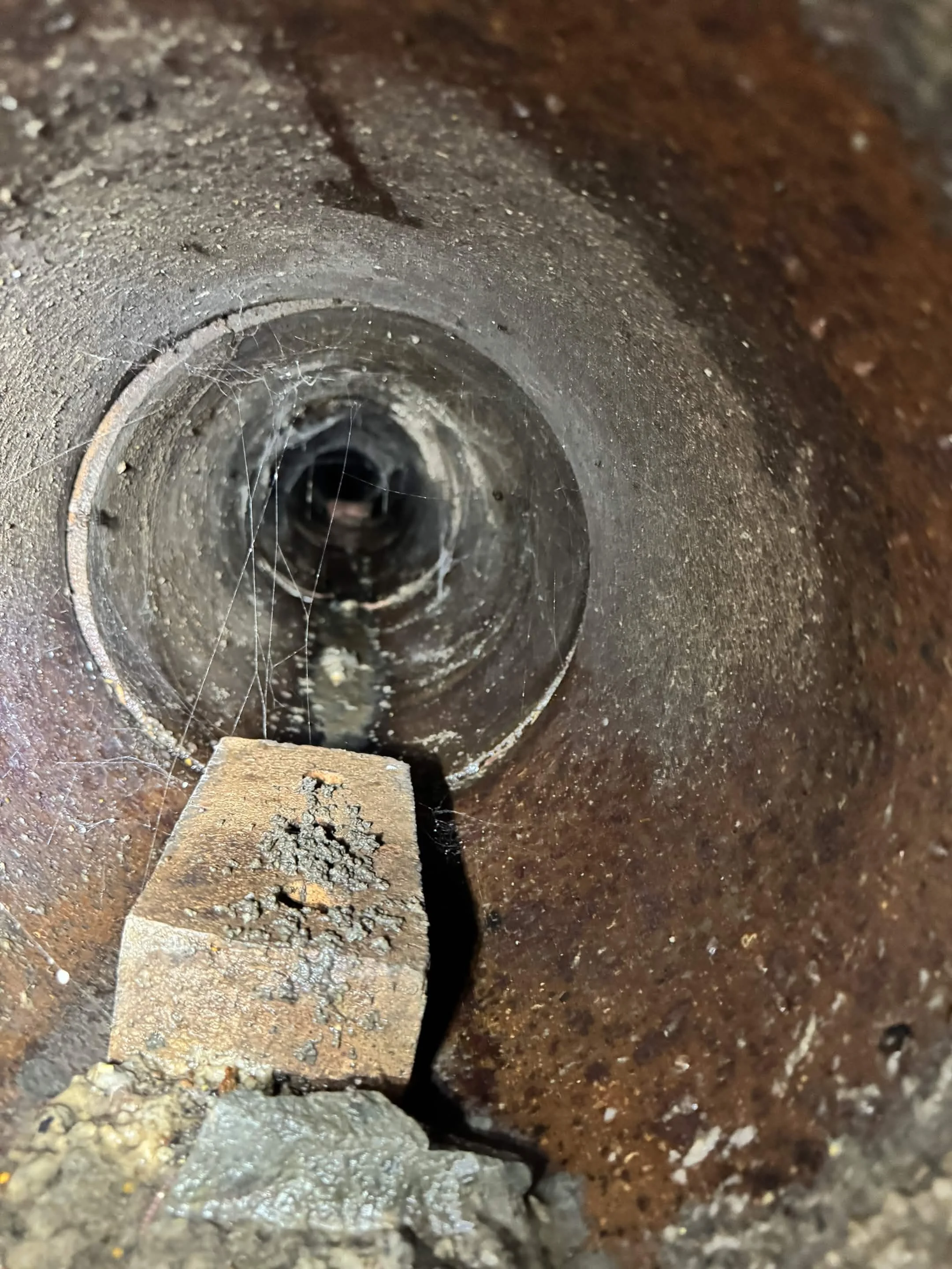 Inside view of a rusty metal pipe or hole with cobwebs and debris inside.