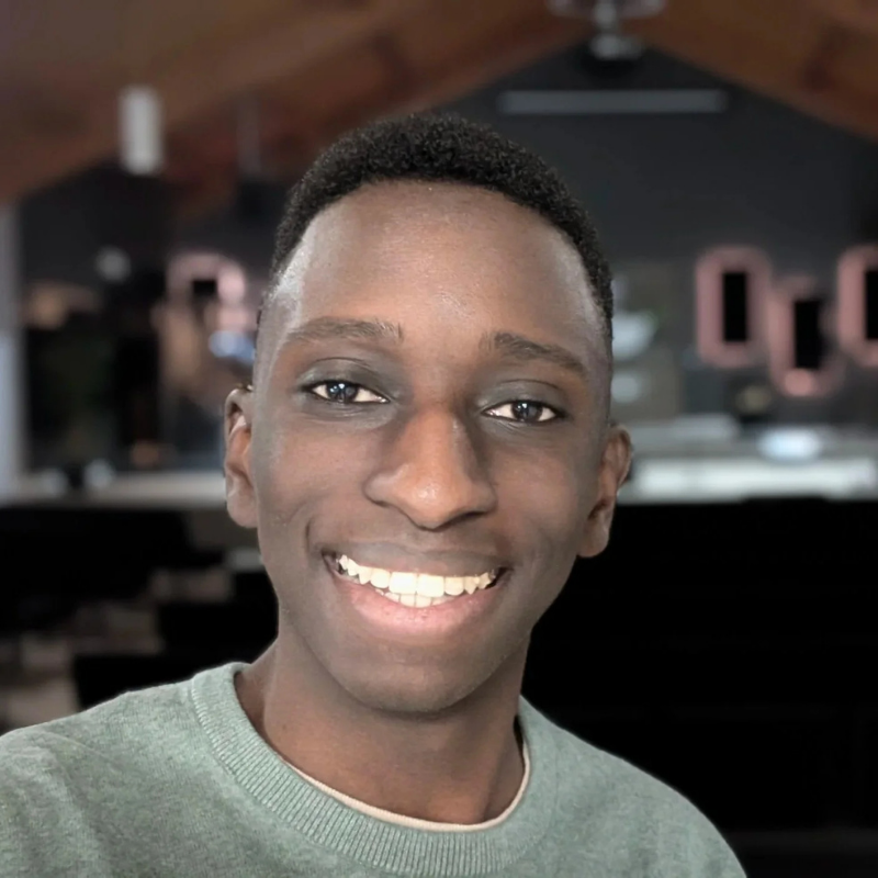 Smiling young man taking a selfie in an indoor setting with a wooden ceiling and dark background.